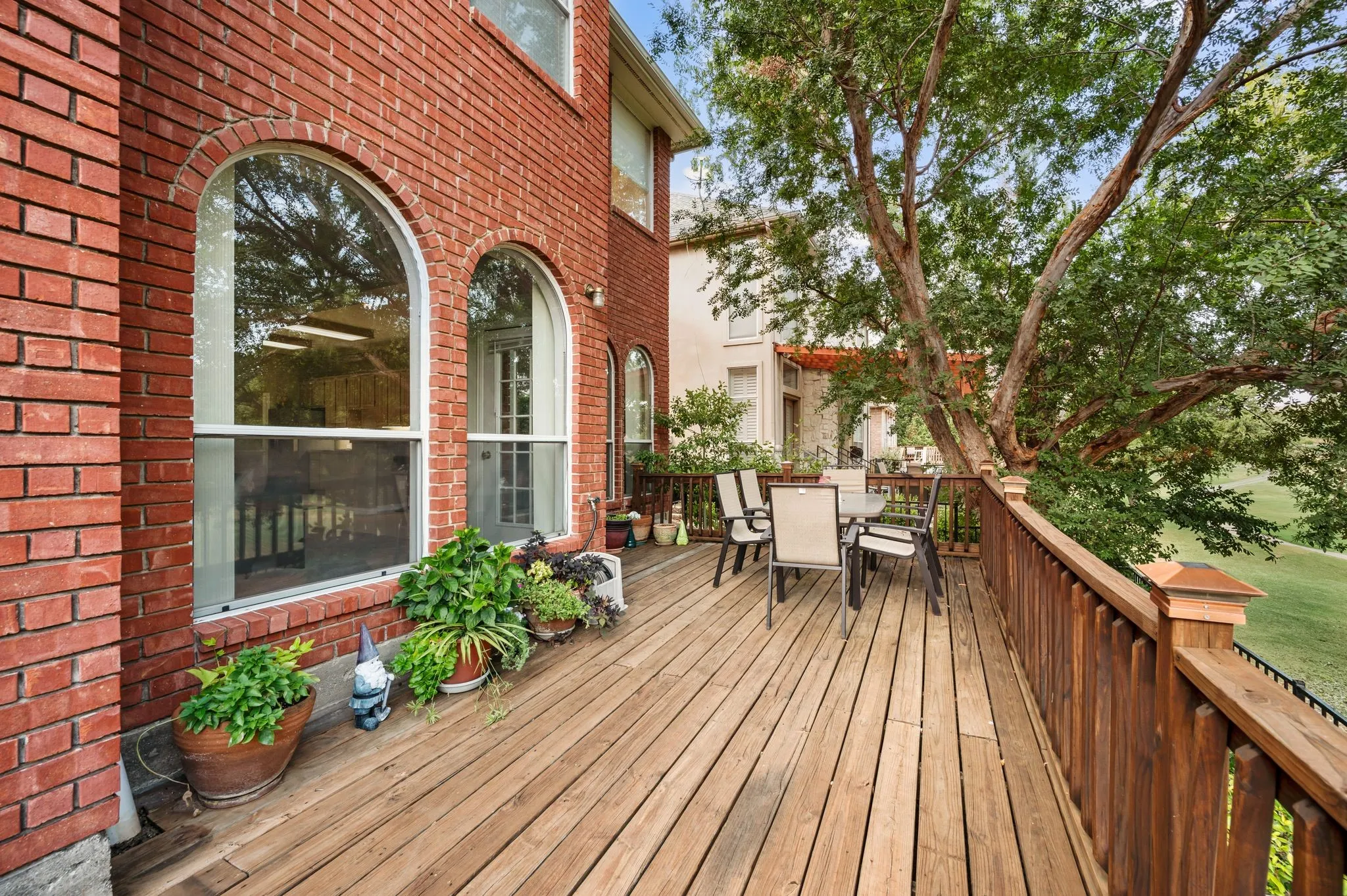 Expansive wood-finish deck with a wood railing, brick exterior, and arched windows