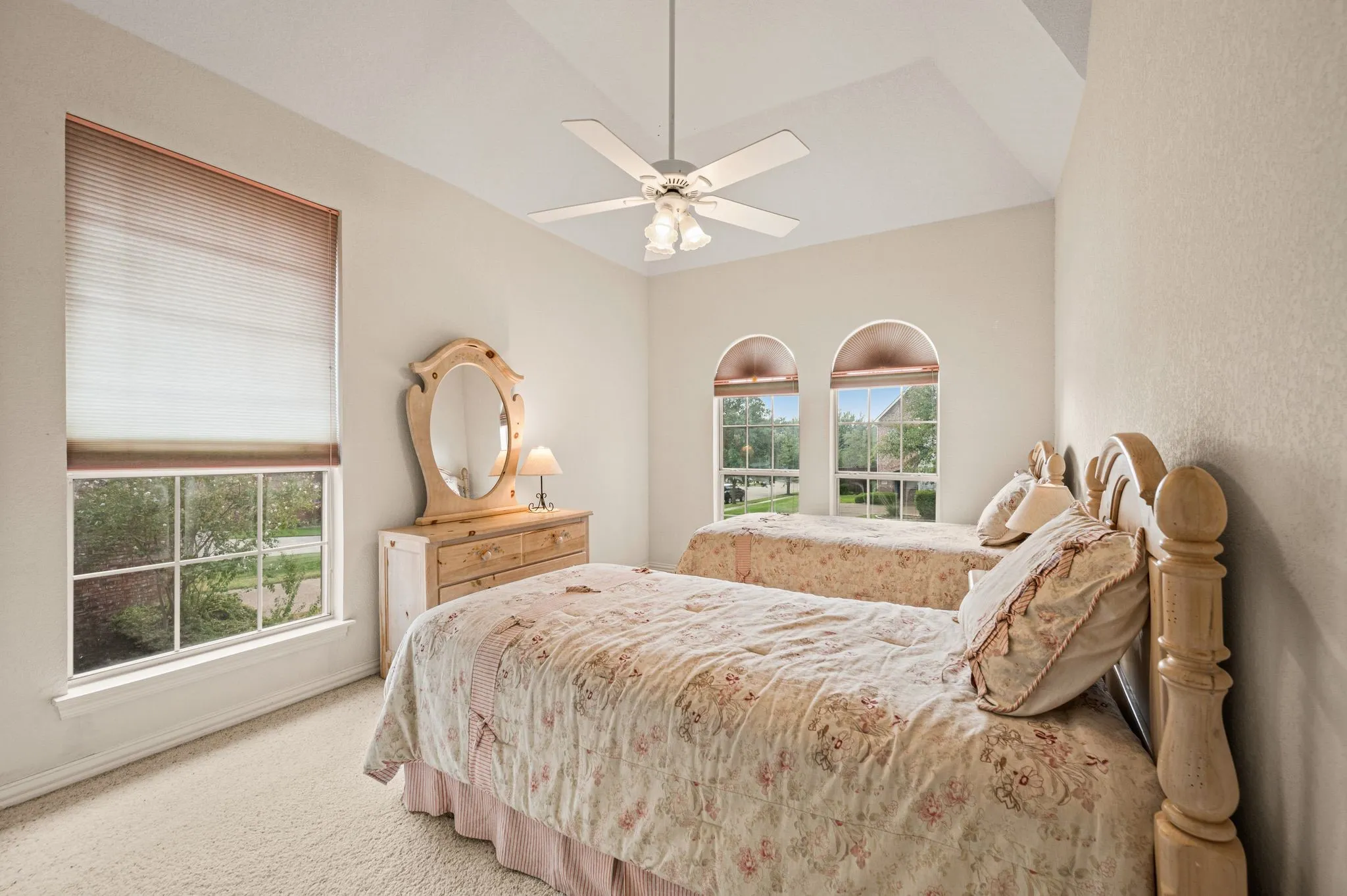 Vaulted ceiling with a ceiling fan, arched windows, rectangular window with gridded panes, and light-toned carpeting