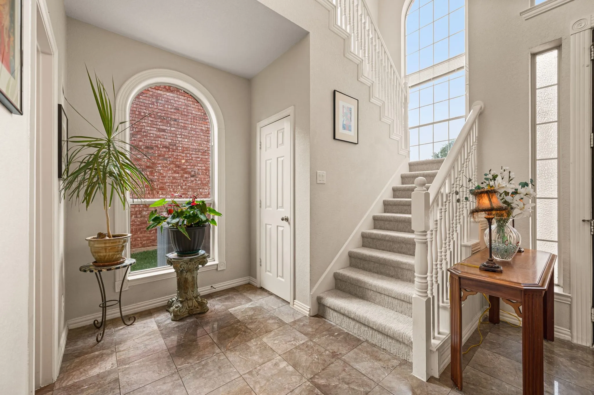 Two-story entryway featuring a carpeted staircase with white balusters, a large arched window, tiled flooring, and a paneled door