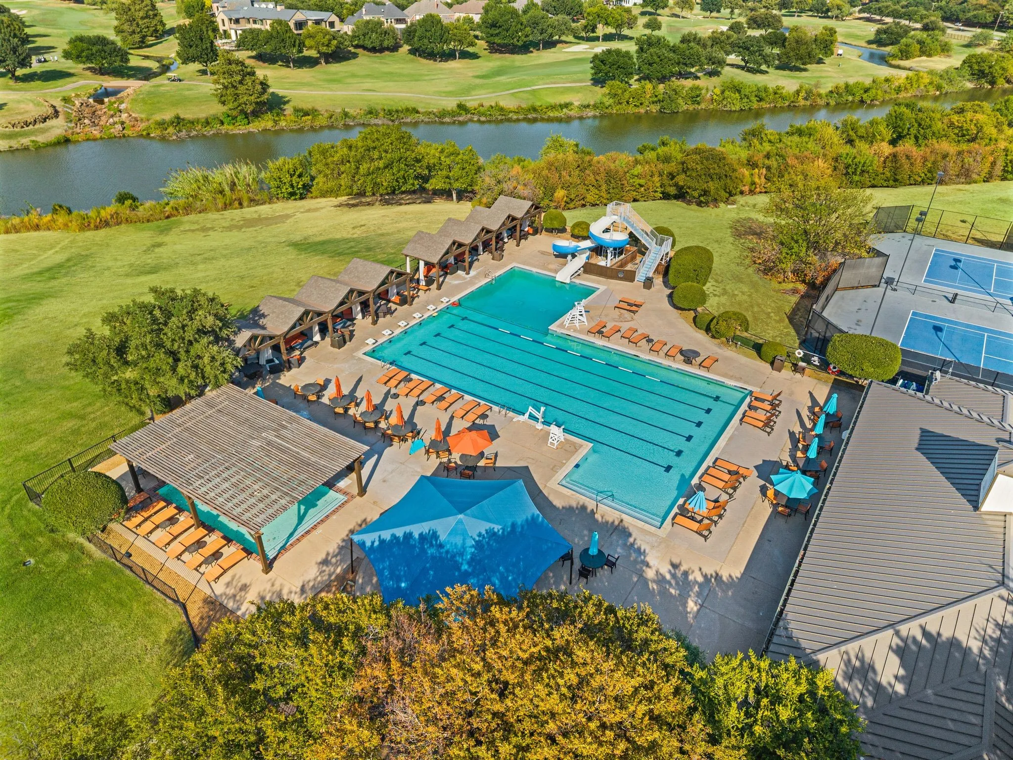 Expansive outdoor swimming pool with lap lanes, adjacent covered cabanas, and a water slide feature