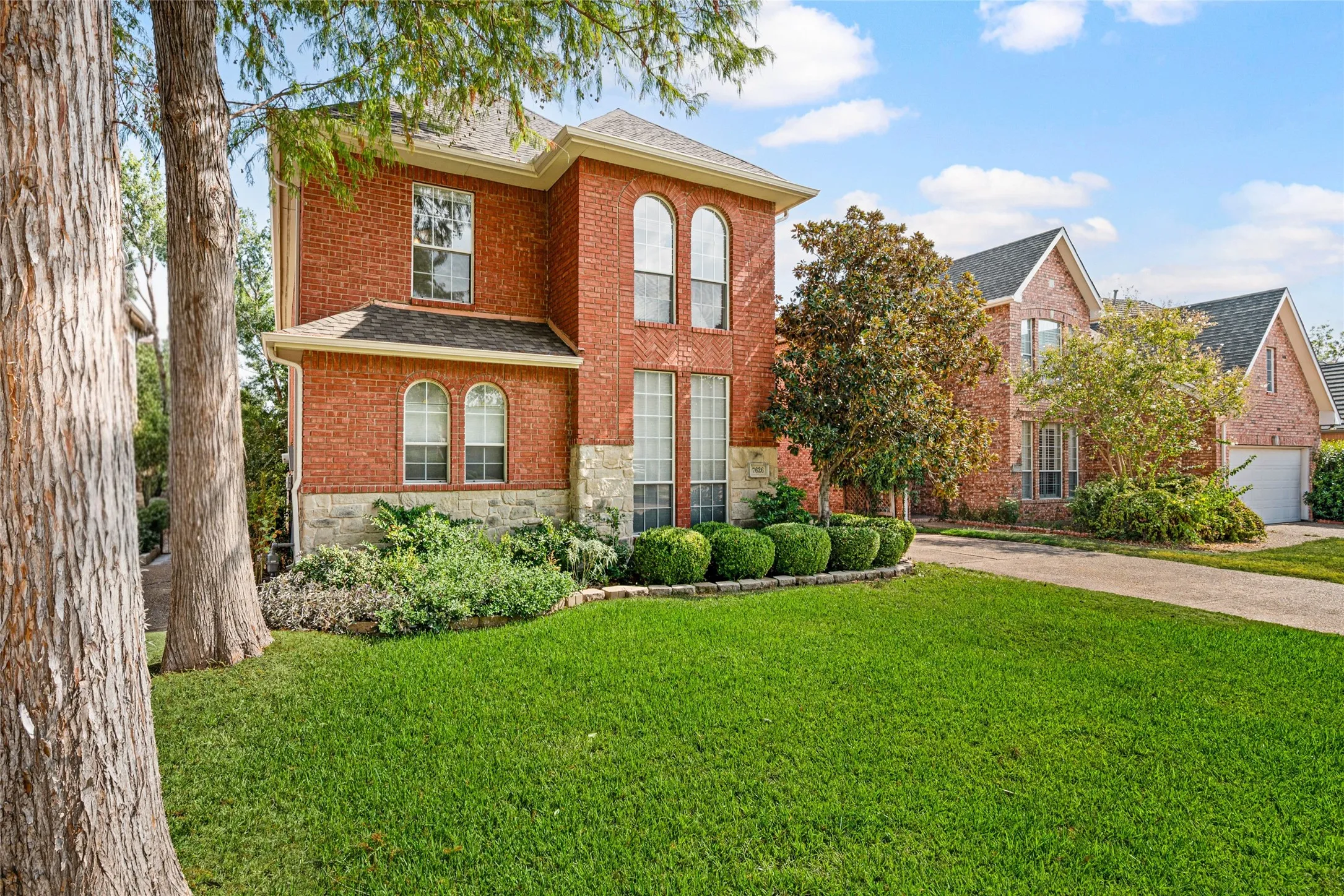 Brick exterior with stone accents, arched windows, gabled roofline, and established landscaping