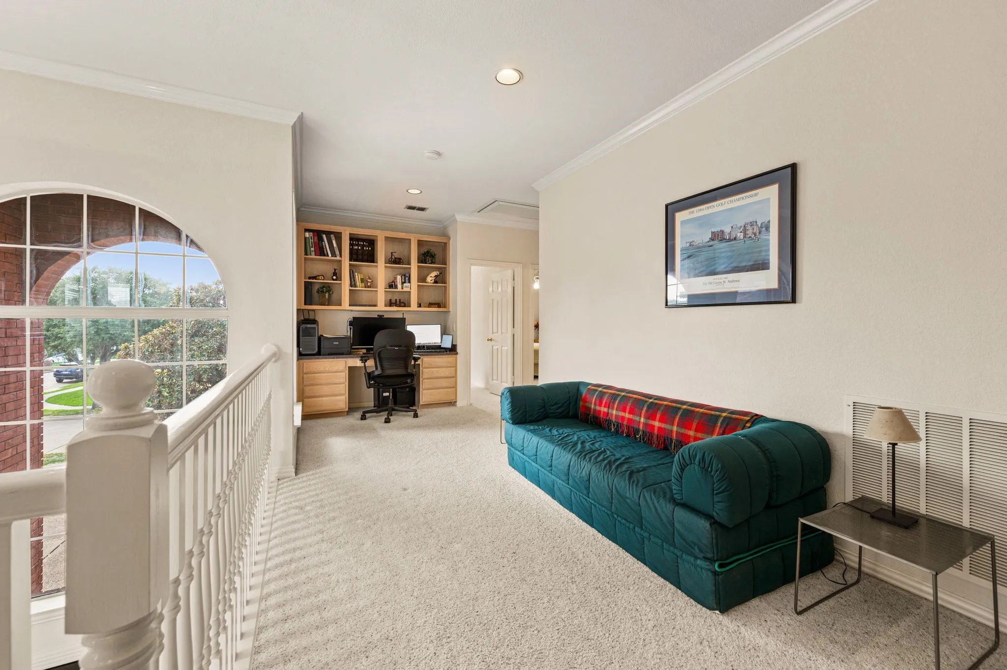 Arched window with gridded panes, built-in desk, built-in shelving, carpet flooring, and crown molding