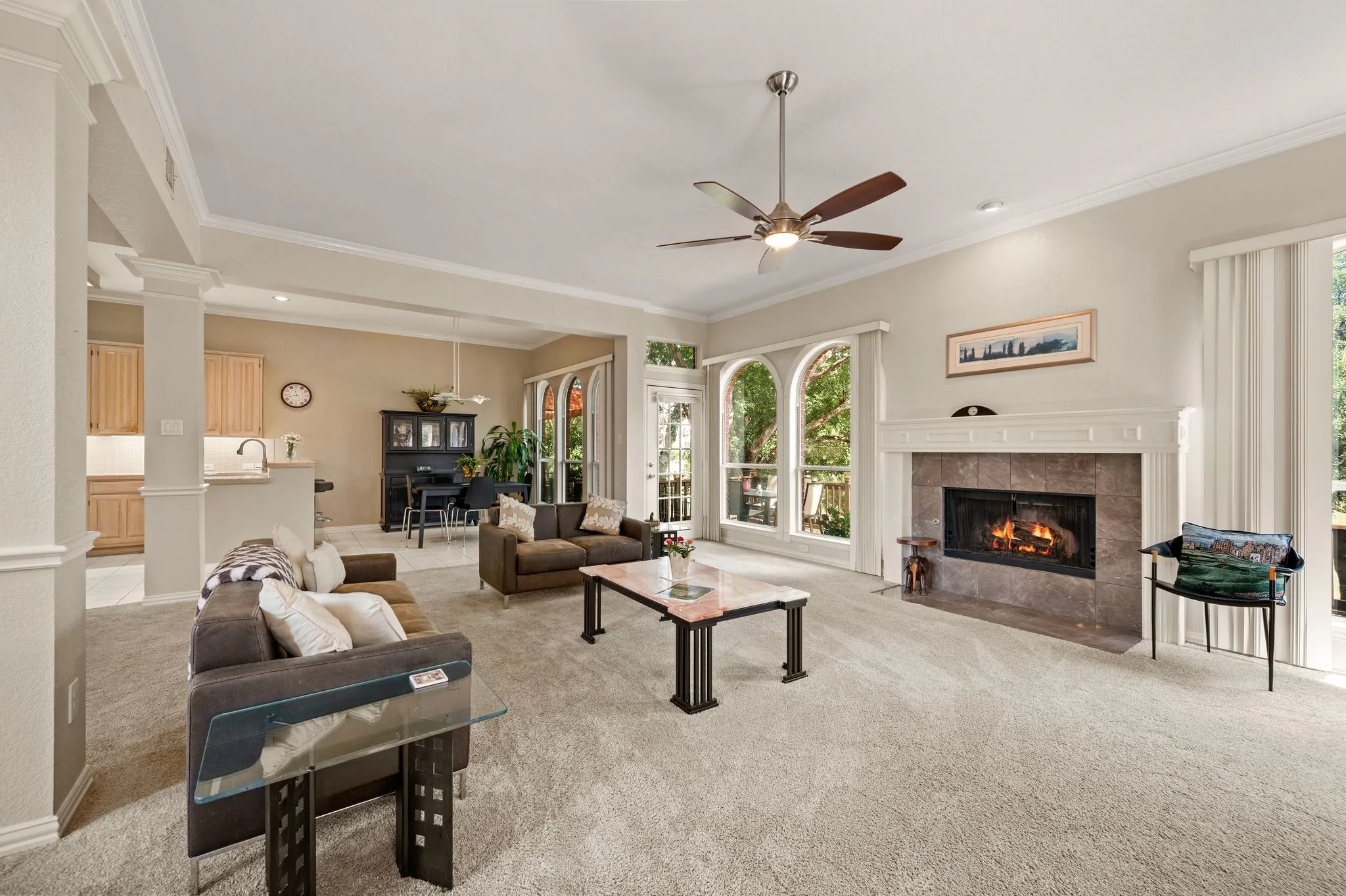 Spacious living area featuring a stone fireplace with a substantial mantel, arched windows, and a ceiling fan