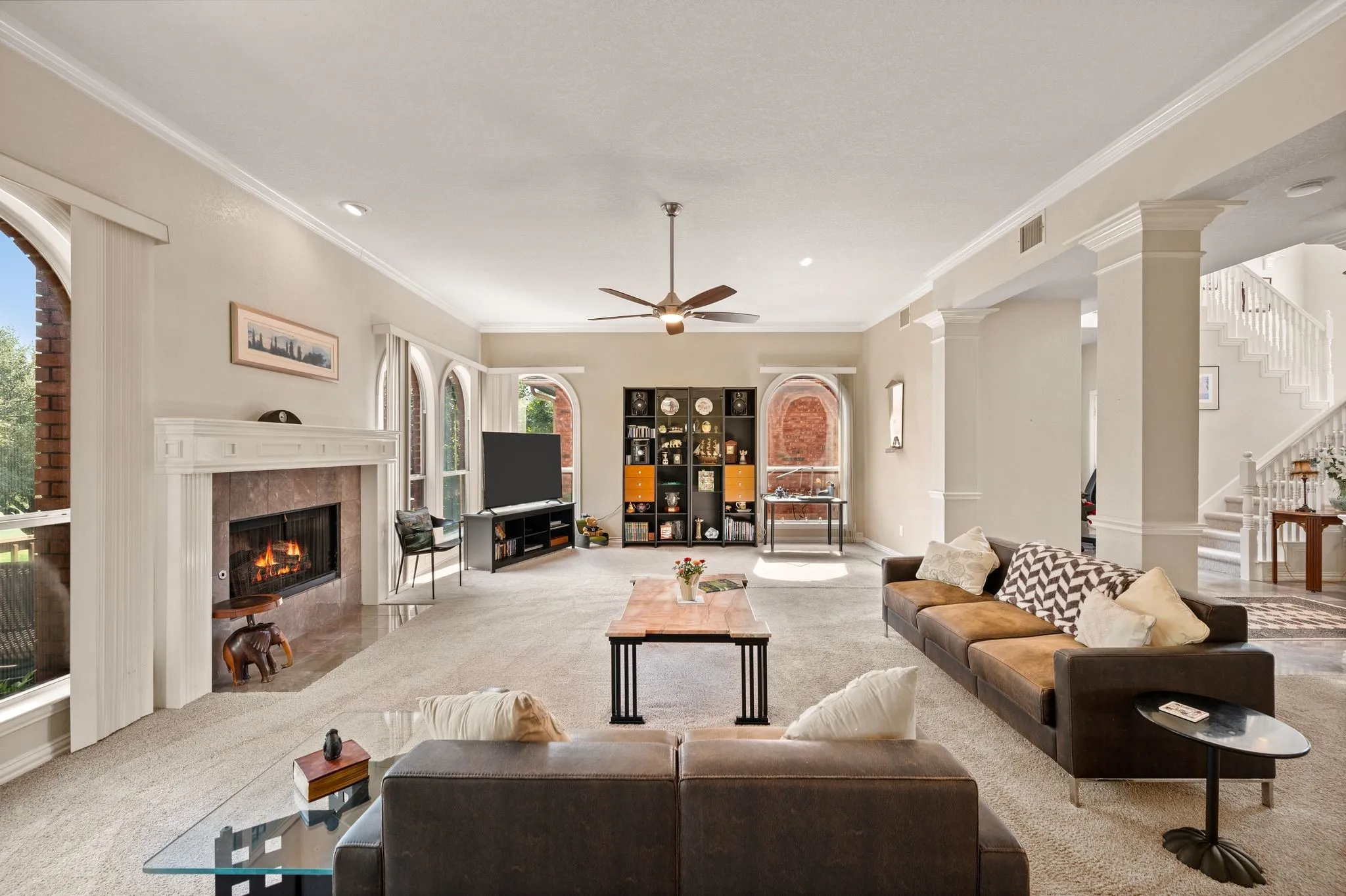 Spacious living area featuring a fireplace with a stone surround, arched windows, decorative columns, and crown molding