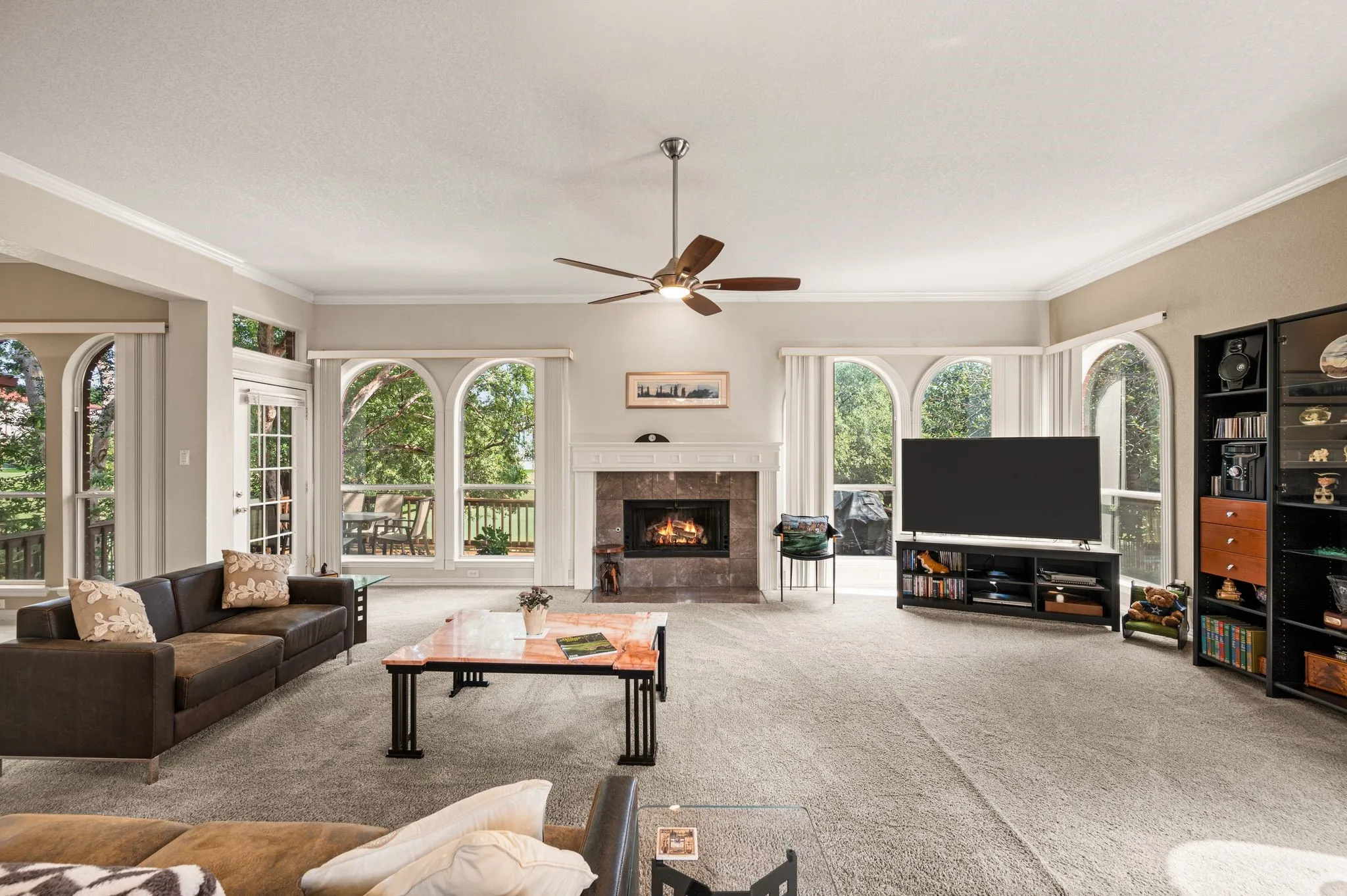 Spacious living area featuring a stone-clad fireplace, multiple arched windows, a ceiling fan, and carpeted flooring