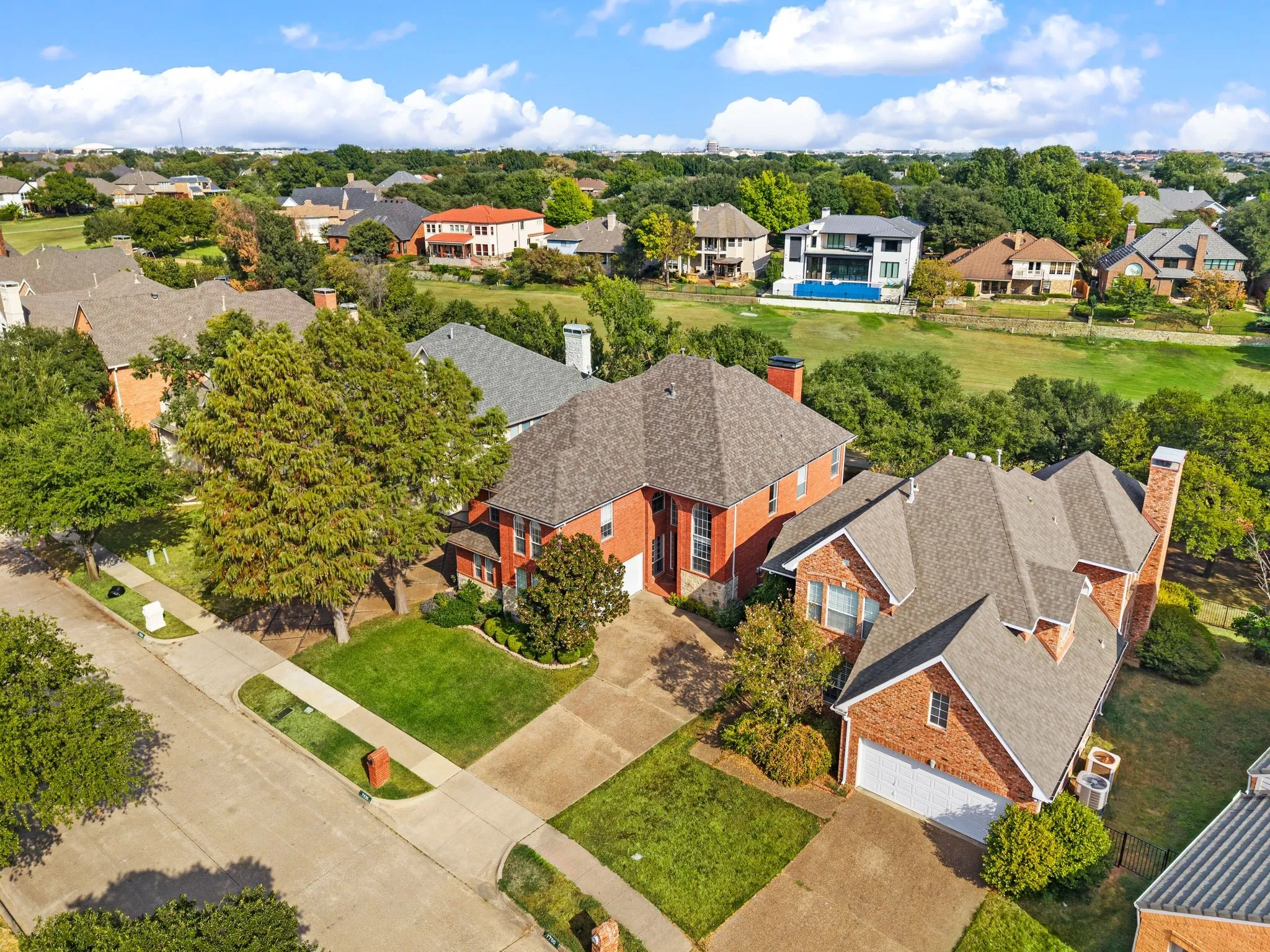 Brick exterior with an attached garage, gray shingle roofing, and a manicured lawn