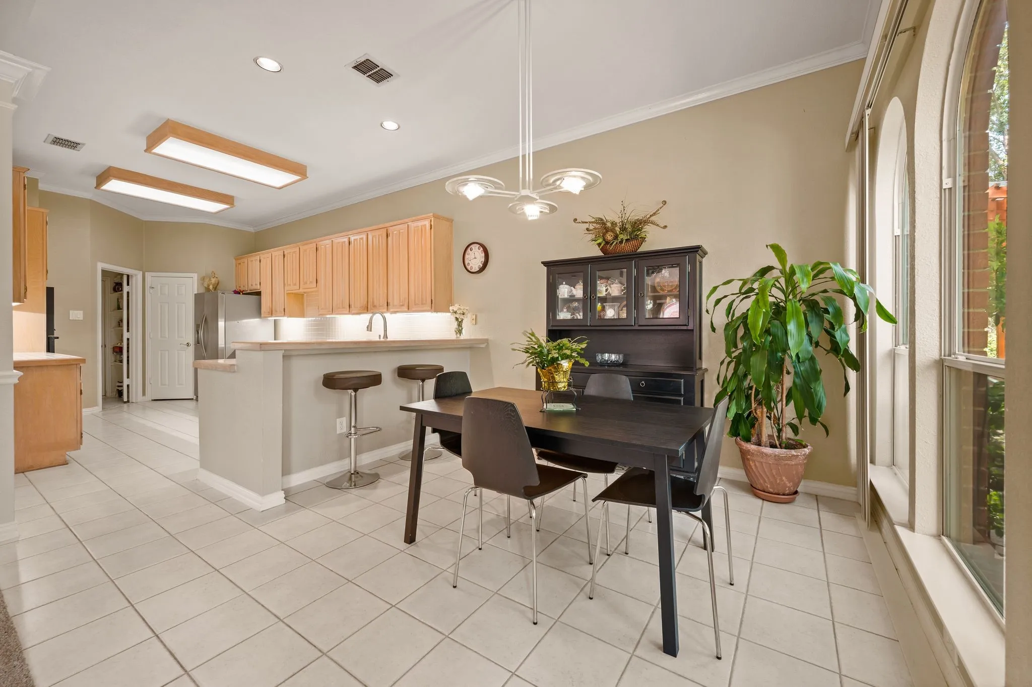 Tile flooring throughout, kitchen with light wood cabinetry, breakfast bar with seating, recessed lighting, and arched windows