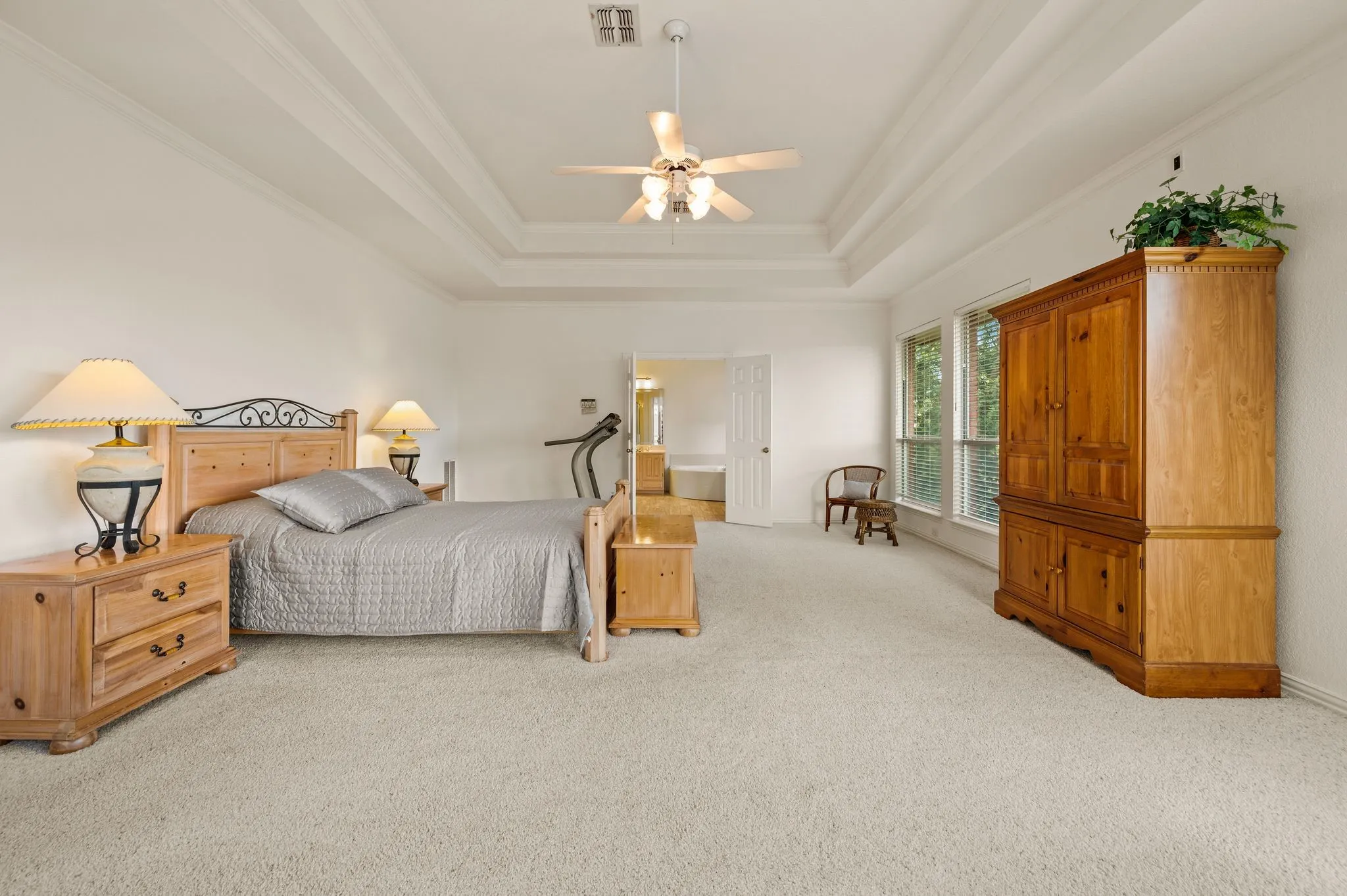Tray ceiling with crown molding, ceiling fan with light fixture, light-toned carpeting, and multiple windows