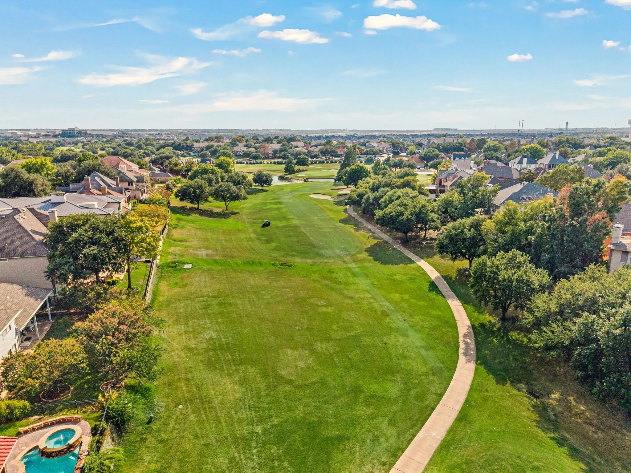 Expansive golf course frontage with a paved cart path, mature trees bordering the fairway, and a distant water feature on the course