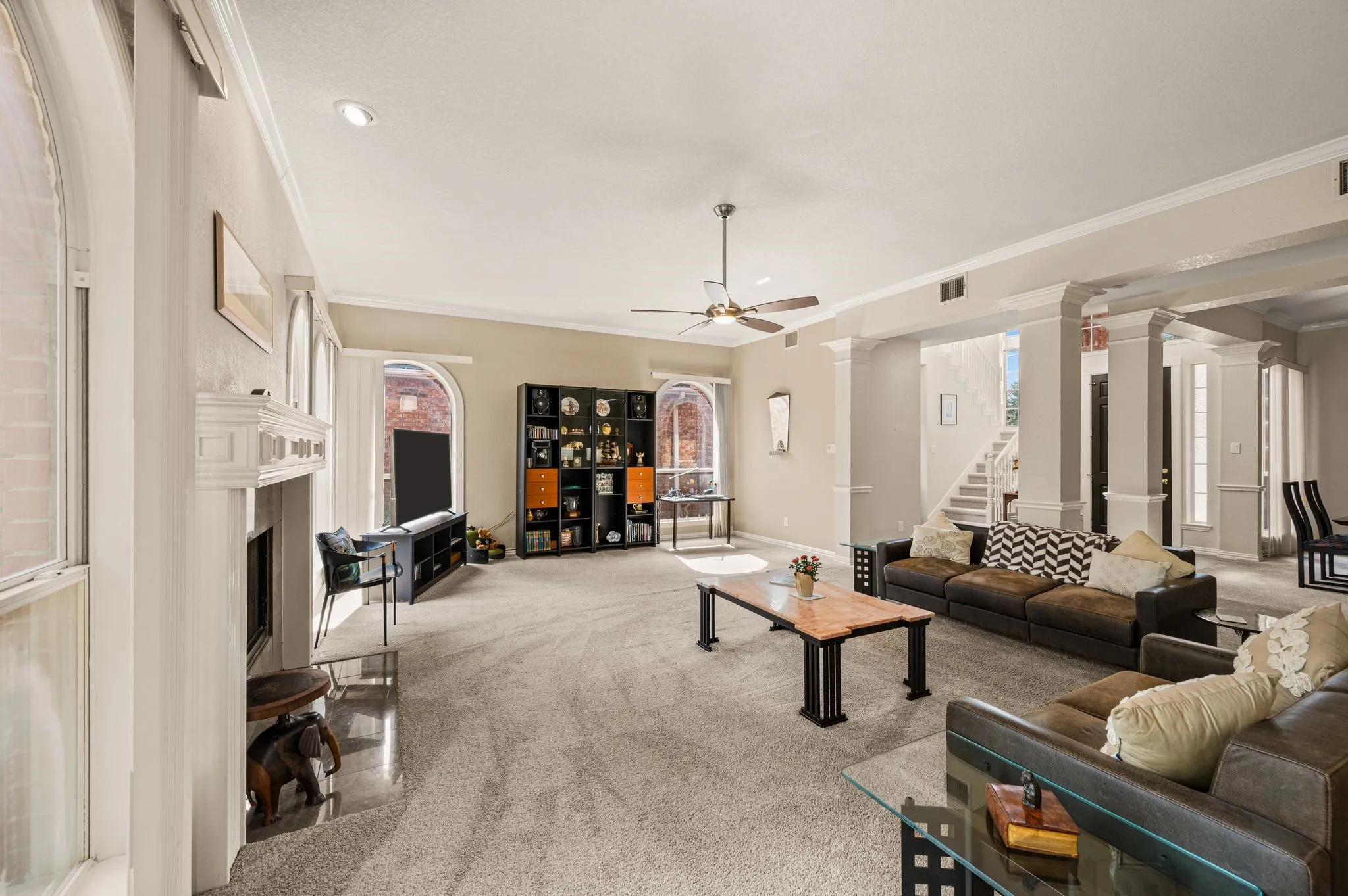 Spacious living area featuring carpet flooring, a fireplace with a detailed mantel, and multiple arched windows