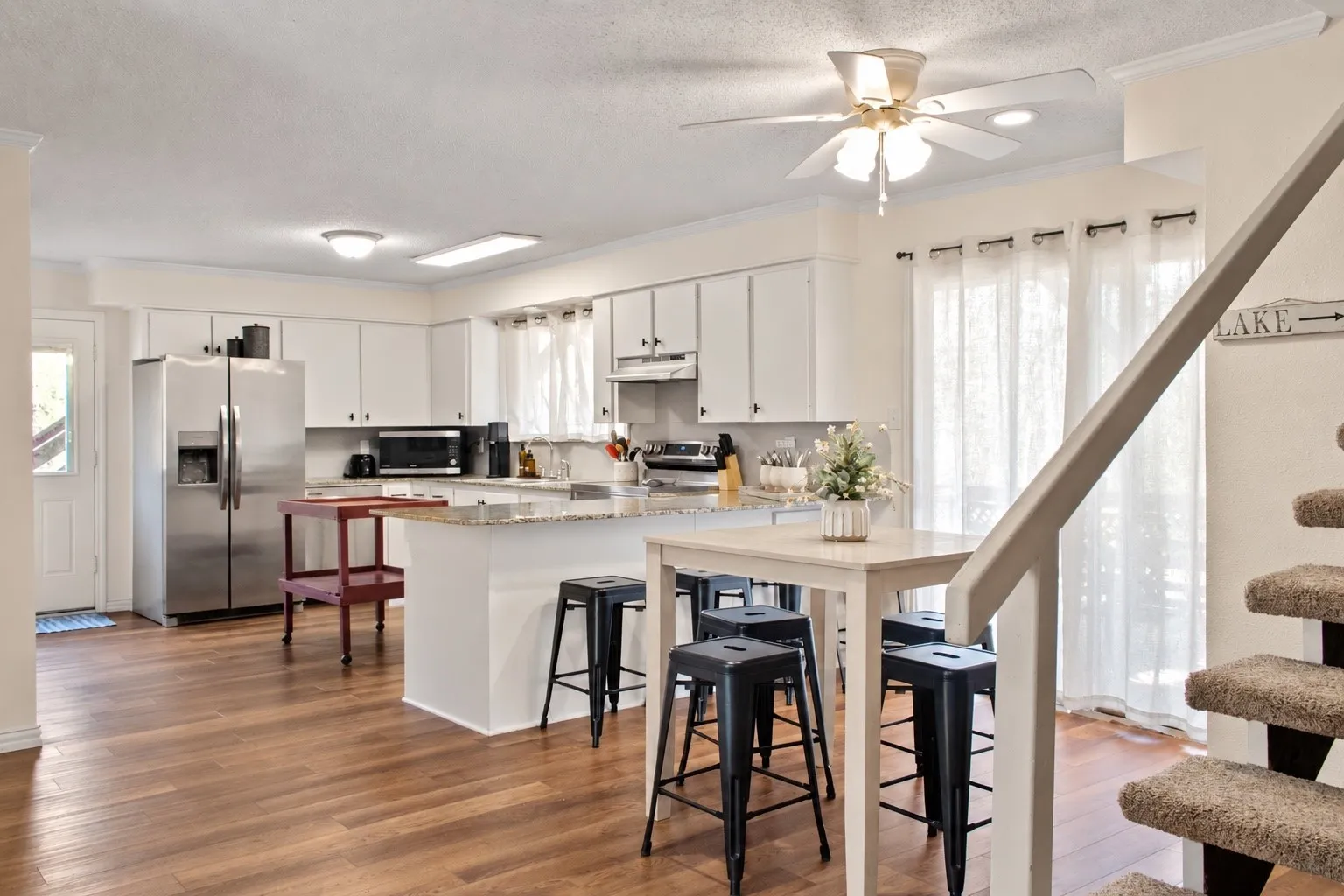 Kitchen featuring stainless steel appliances, white cabinetry, a kitchen island with seating, a ceiling fan, and wood-finish flooring