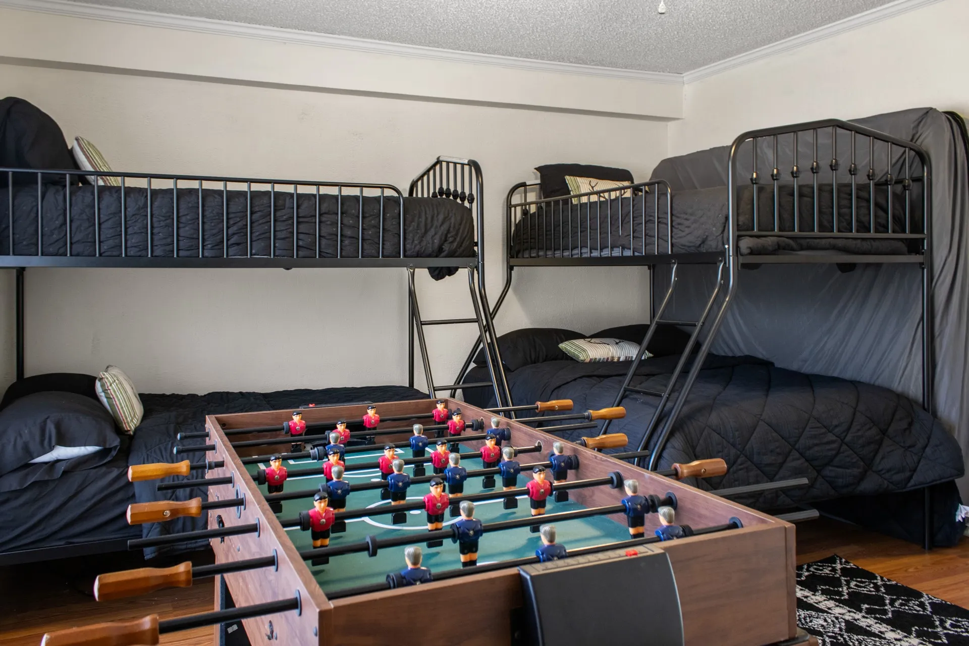 Room featuring two metal bunk beds, wood-finish flooring, and a foosball table