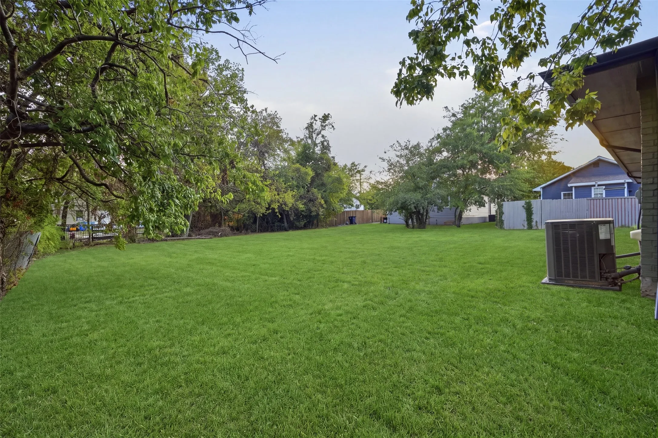 Expansive grass lawn with mature trees and partial fencing