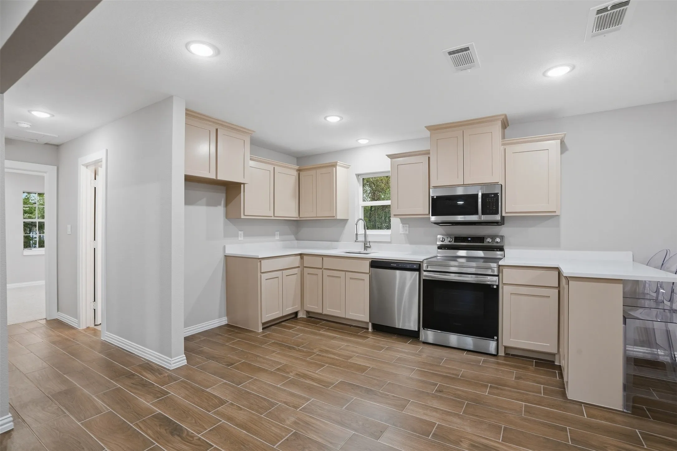 Kitchen featuring wood-finish tile flooring, recessed lighting, light-toned cabinetry, white countertops, and stainless steel appliances