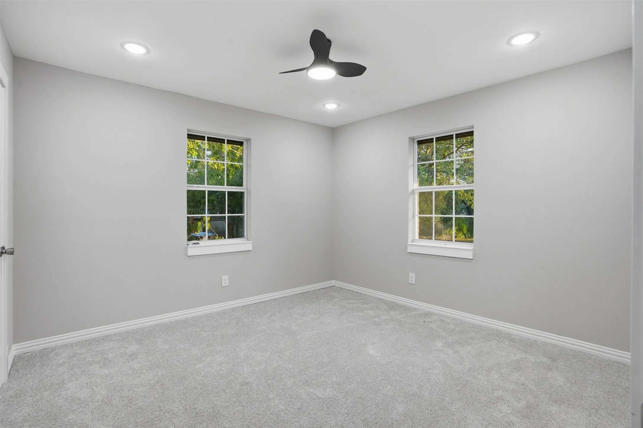 Recessed ceiling lighting, ceiling fan, two double-hung windows, light gray carpet, and white trim