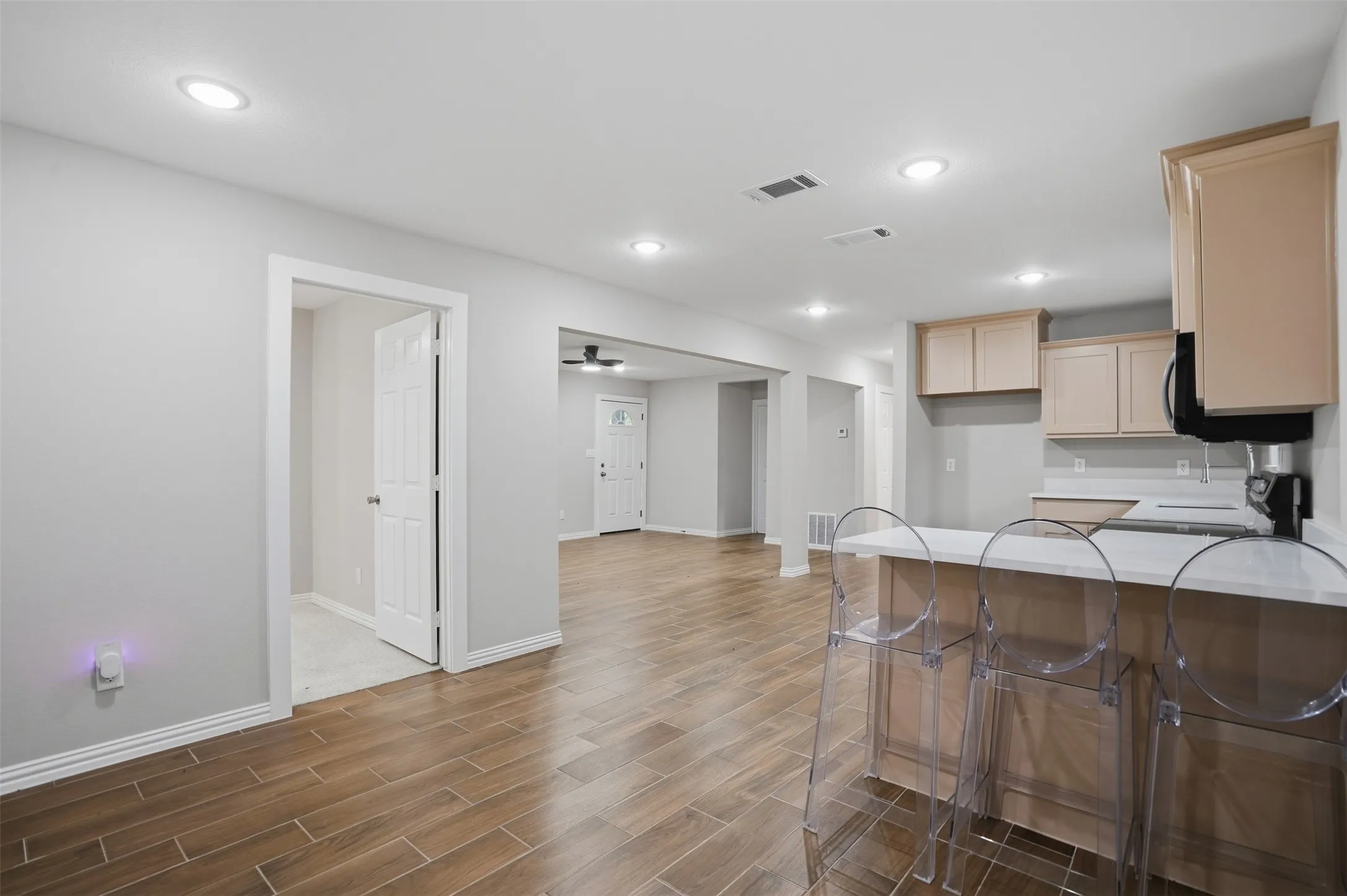 Open concept living area featuring wood-finish flooring, recessed lighting, and a kitchen with light-toned cabinetry and a breakfast bar