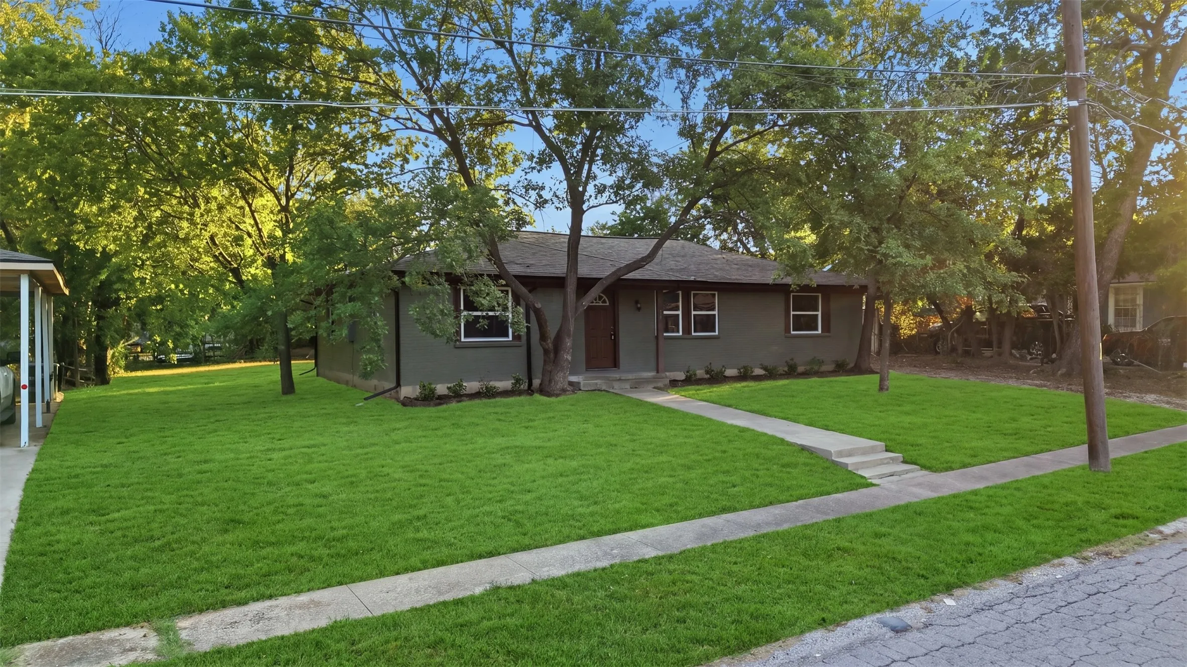 Smooth stucco exterior, dark trim windows, front entry door, established trees, and a manicured lawn