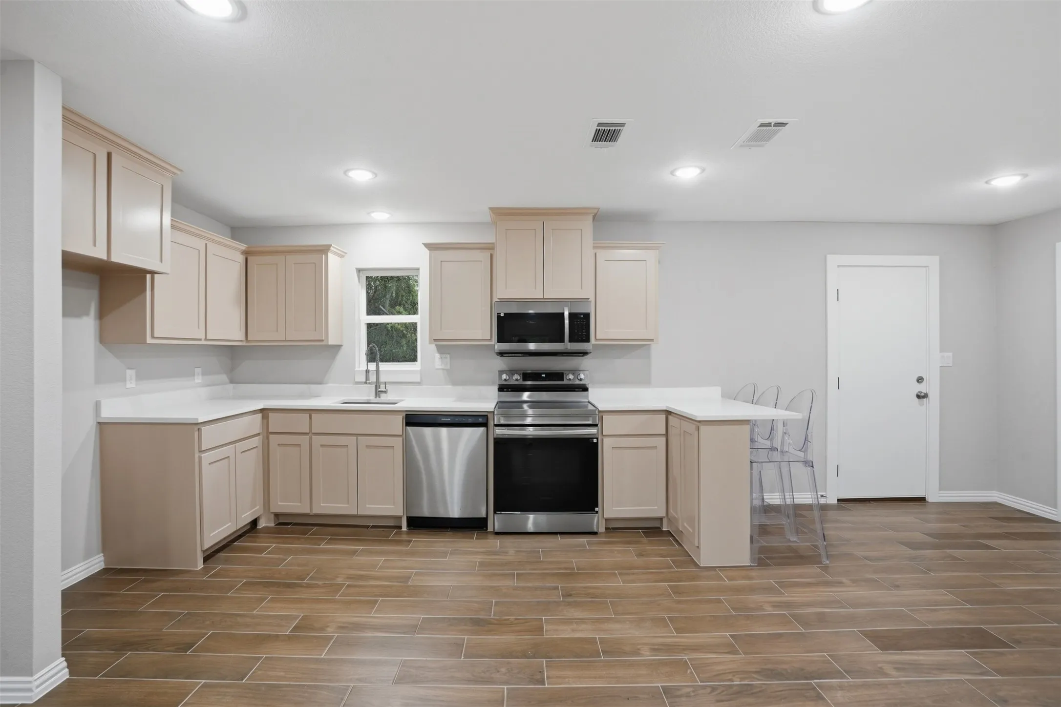 U-shaped kitchen with light-toned cabinetry, stainless steel appliances, and wood-look tile flooring