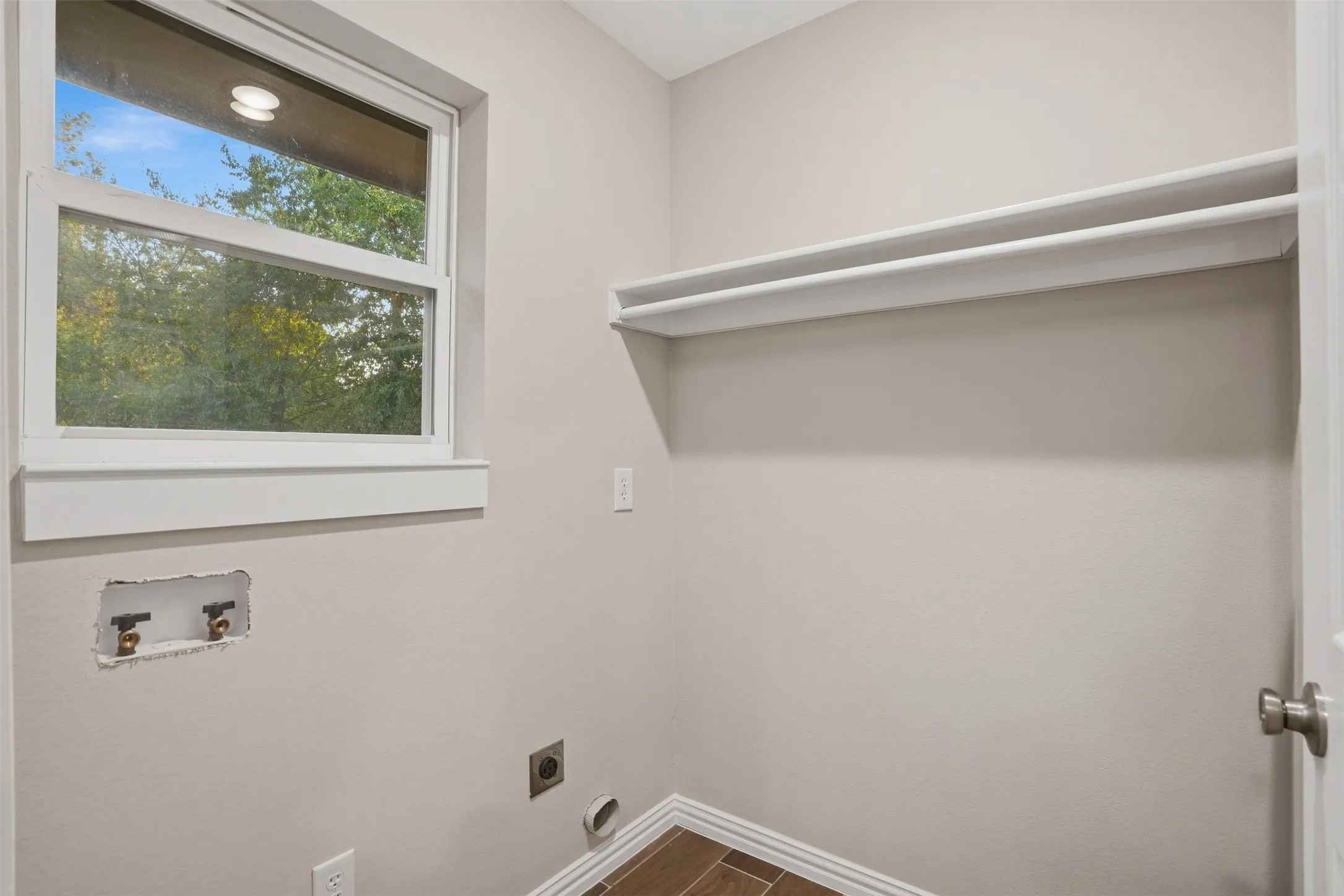 Laundry area featuring a double-hung window, white trim, wood-finish flooring, and a built-in hanging rod