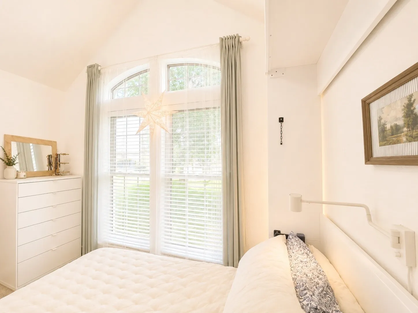 Vaulted ceiling with an arched window, featuring window blinds and soft drapery