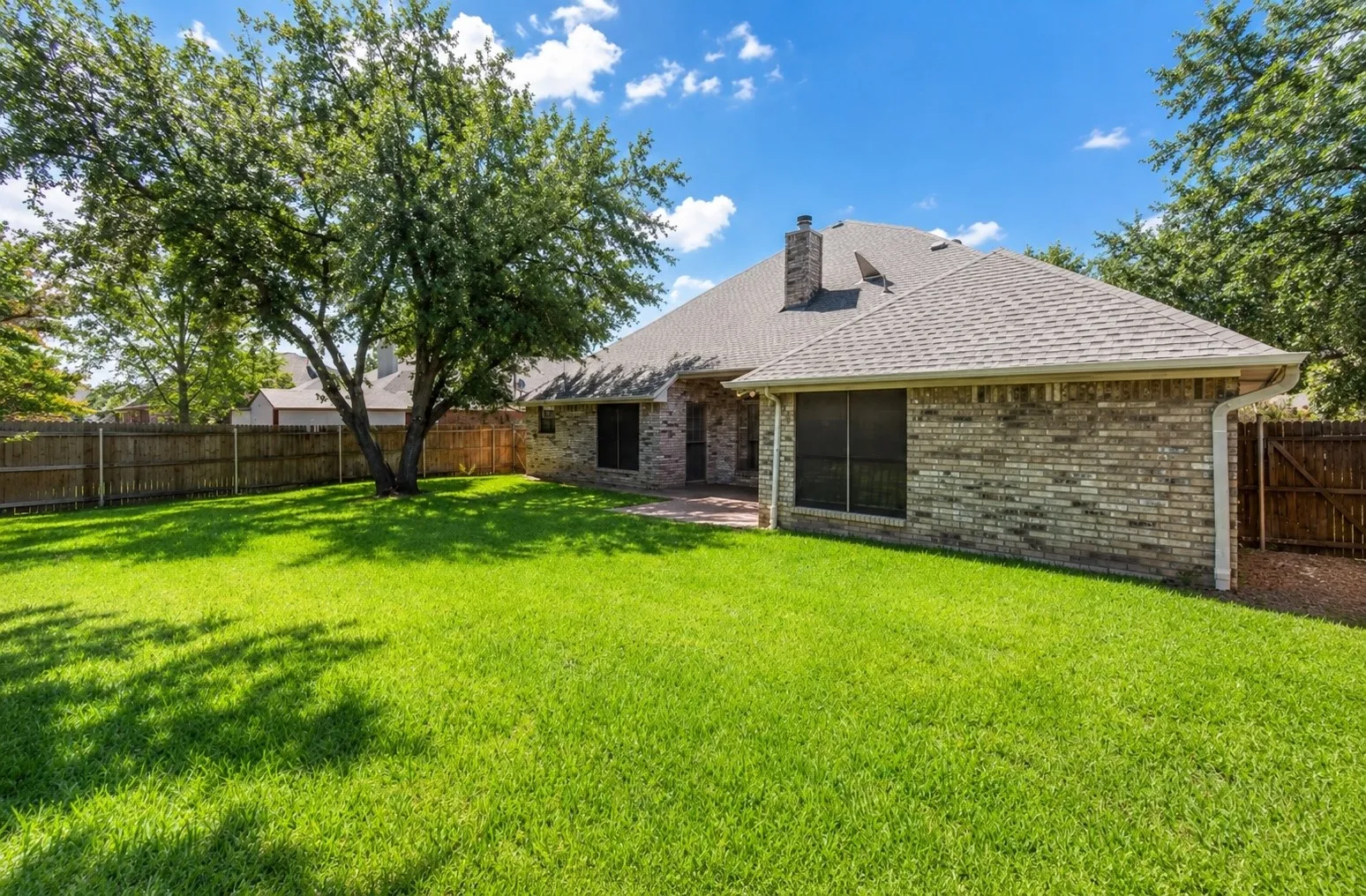 Expansive lawn with a mature shade tree, brick exterior, and privacy fencing