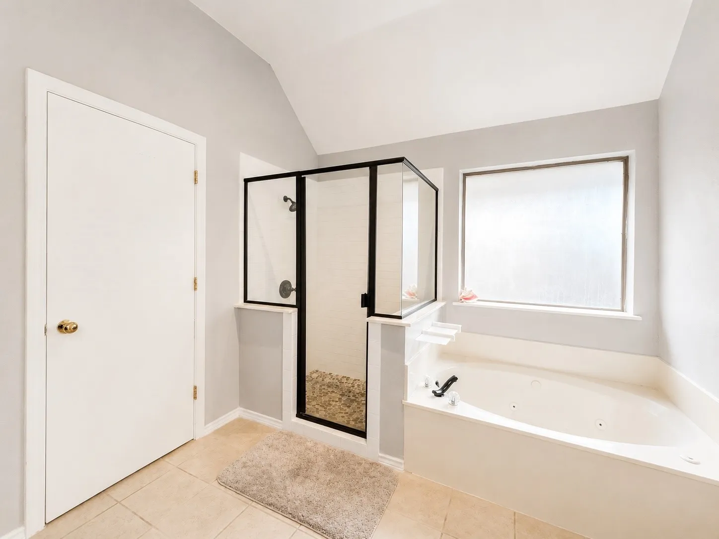 Tiled flooring, jetted soaking tub, glass-enclosed shower with pebble floor, frosted window, and vaulted ceiling