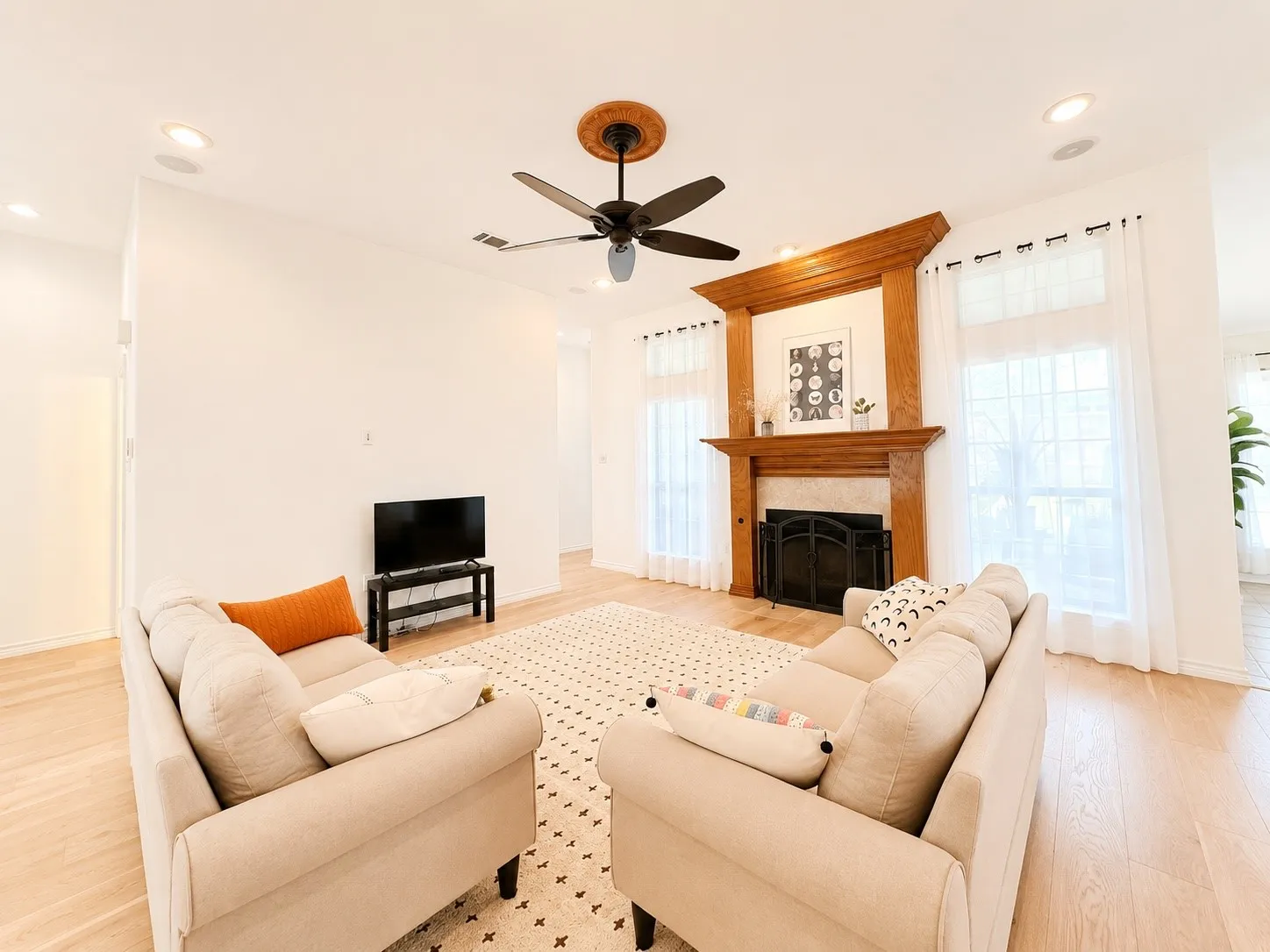 Hardwood flooring throughout, recessed lighting, ceiling fan with light, white walls, and a fireplace with a decorative wood mantel