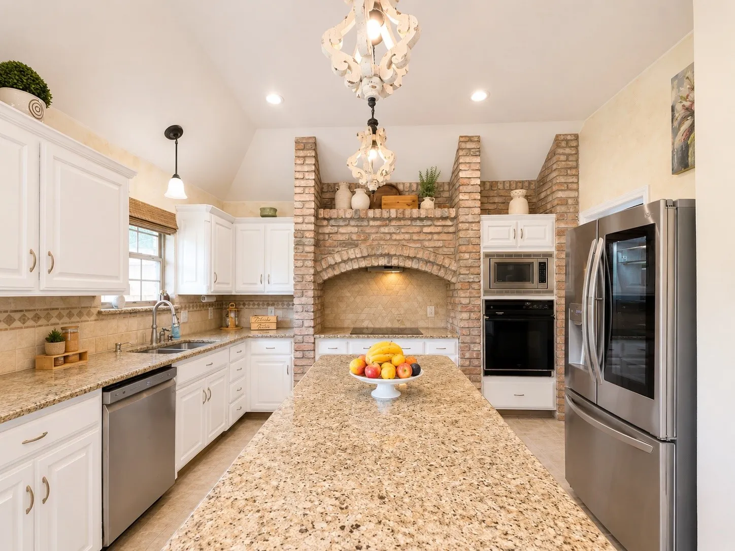 Kitchen featuring a central island with a stone countertop, white cabinetry, stainless steel appliances, brick archway, and decorative light fixtures