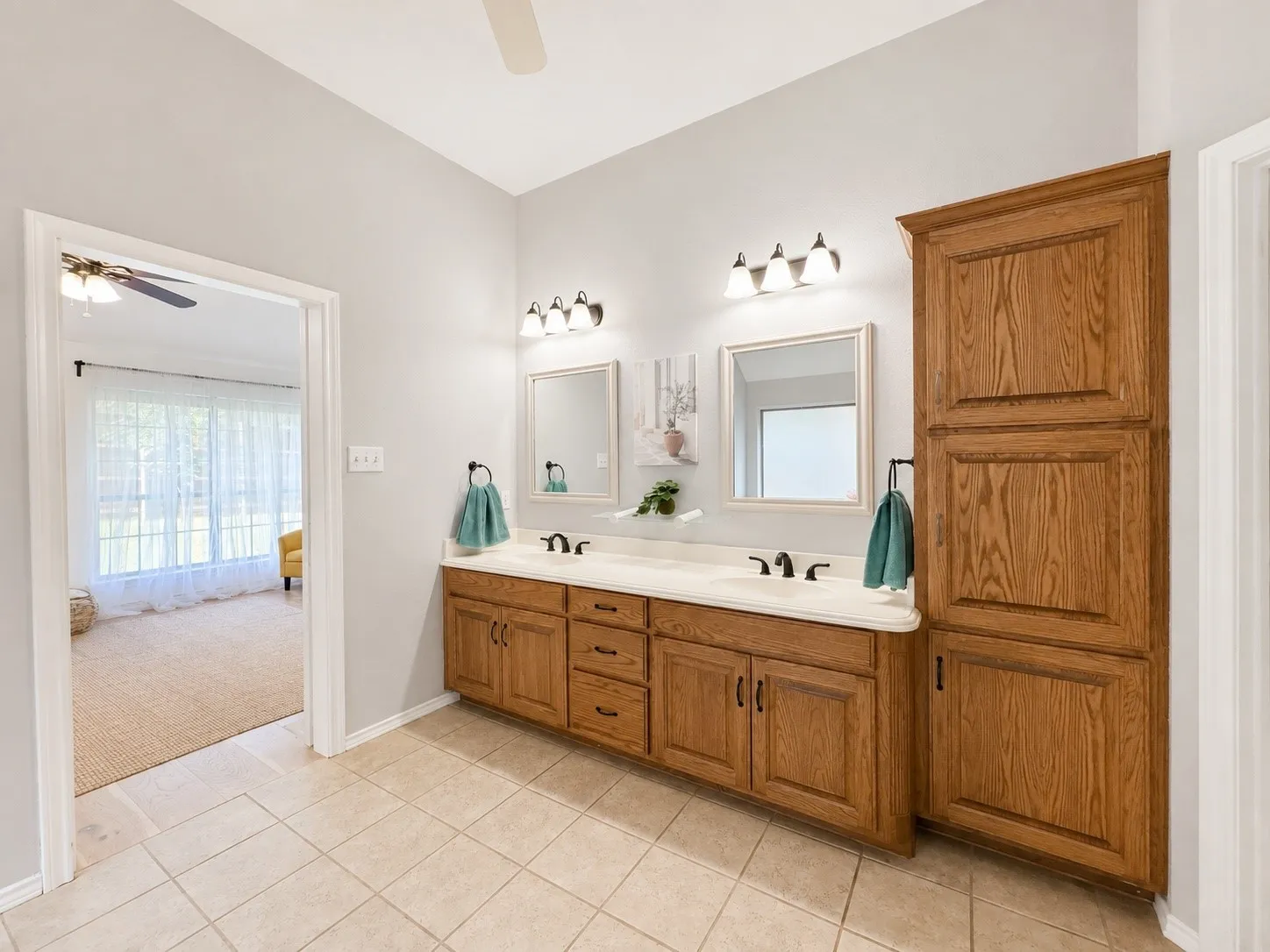 Dual vanity with a light-toned countertop, wood-finish cabinetry, built-in storage, and tiled flooring
