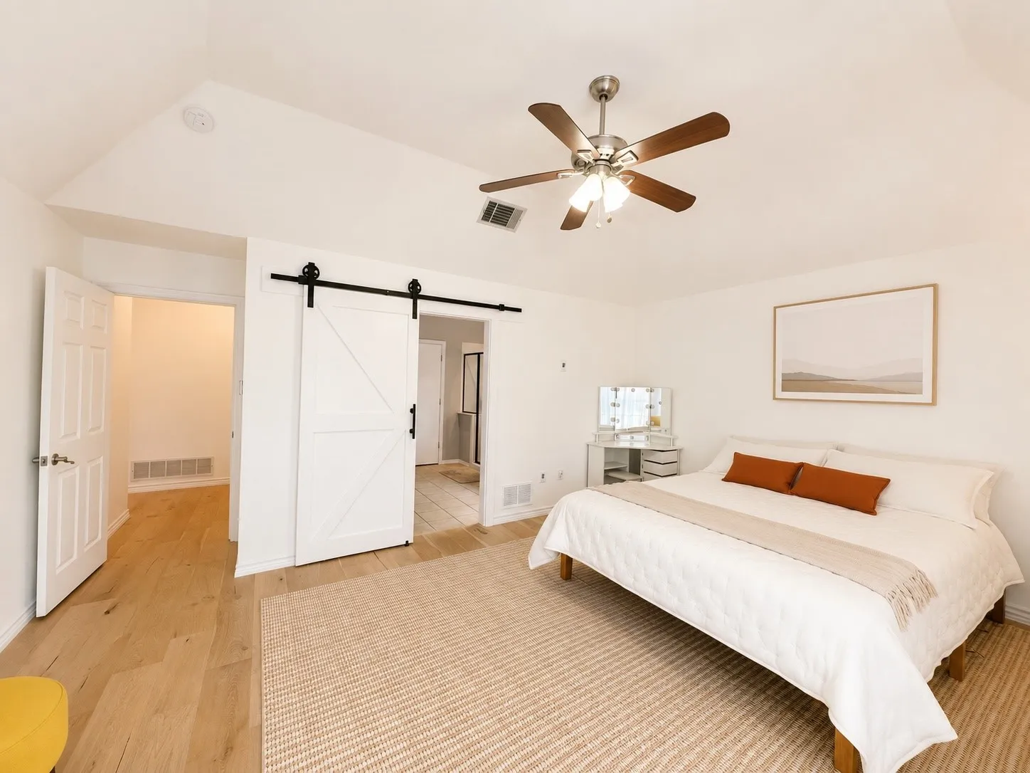 Vaulted ceiling with a ceiling fan, white barn door, wood-finish flooring, and white walls