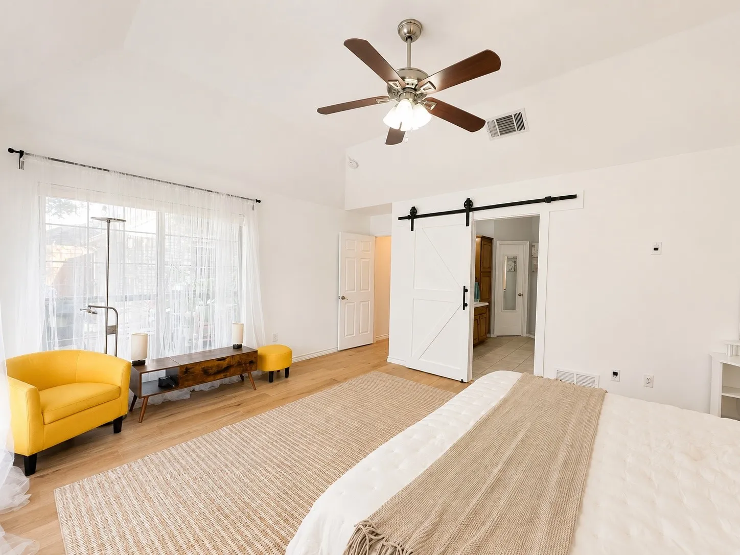 Vaulted ceiling with a ceiling fan, wood-finish flooring, wide window with ample natural light, white barn door, and white walls
