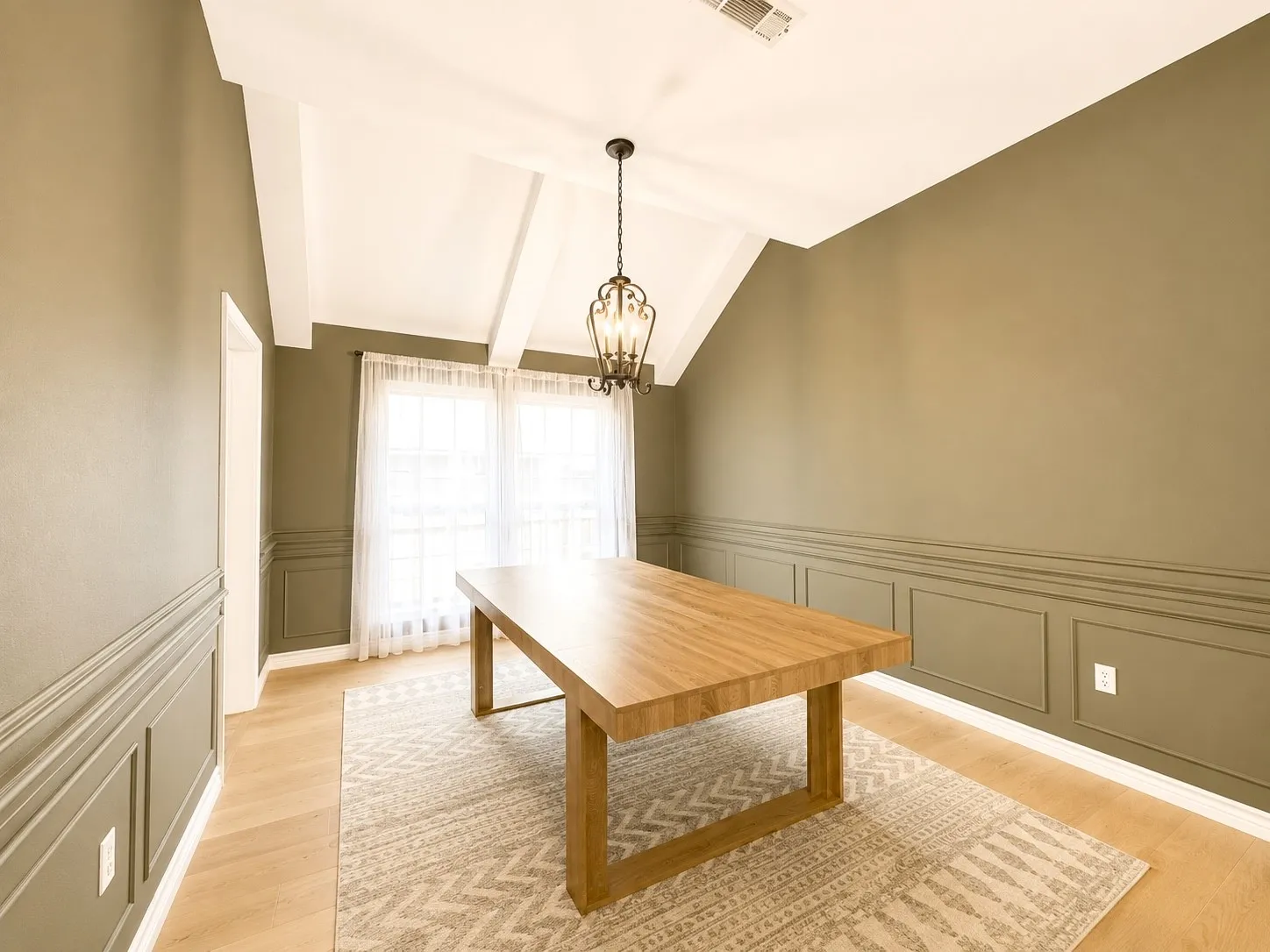 Vaulted ceiling with exposed beams, wood-finish flooring, wainscoting, and a decorative chandelier