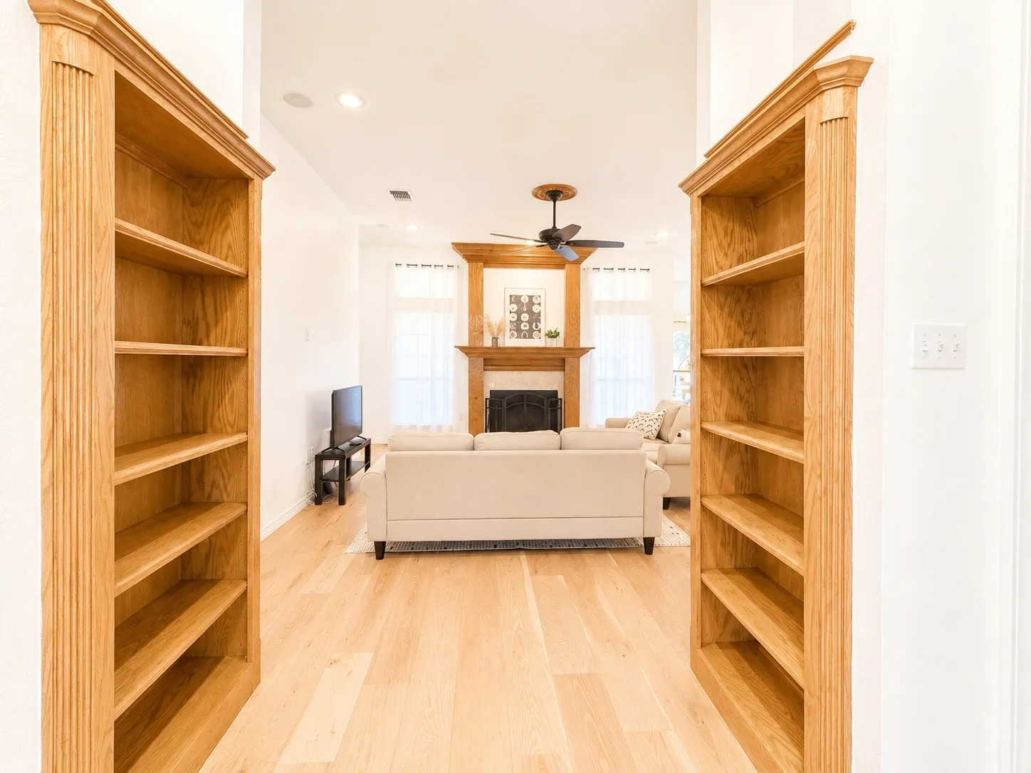 Built-in custom shelving, light wood-finish flooring, recessed ceiling lighting, vaulted ceiling, and a fireplace with a wood mantel