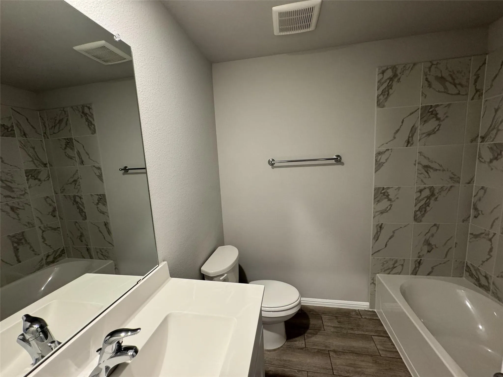 Bathroom featuring a built-in bathtub with tiled surround, wood-finish flooring, and a vanity with an integrated sink