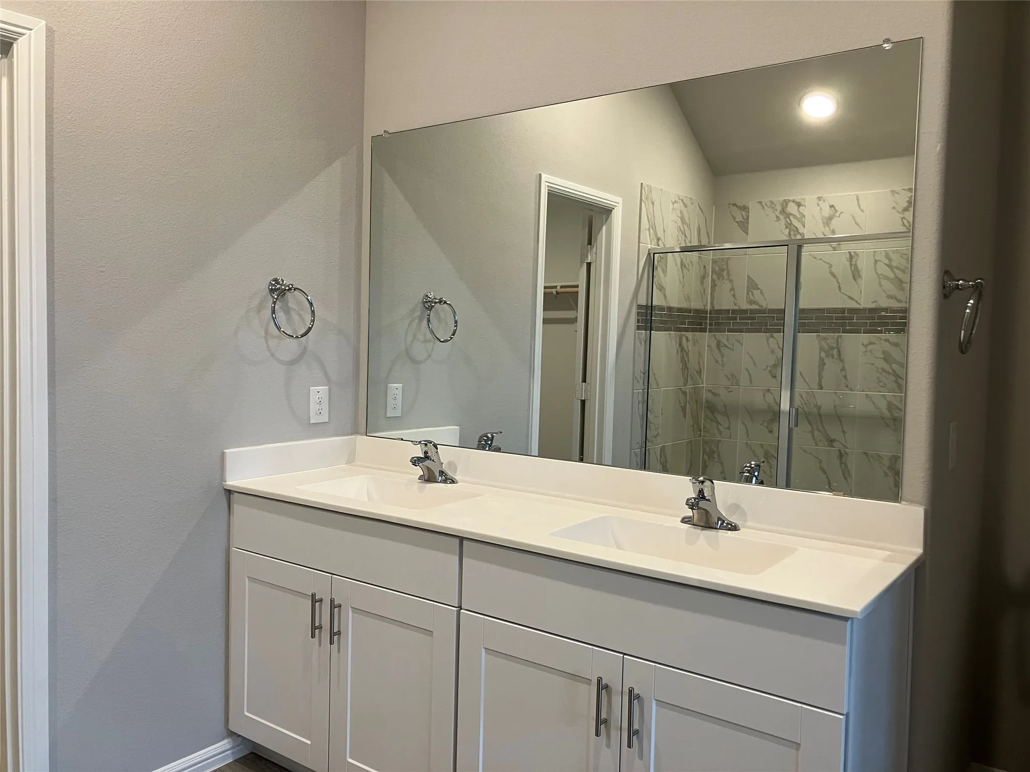 Double vanity with integrated sinks, expansive wall-mounted mirror, light-toned cabinetry, and polished chrome fixtures