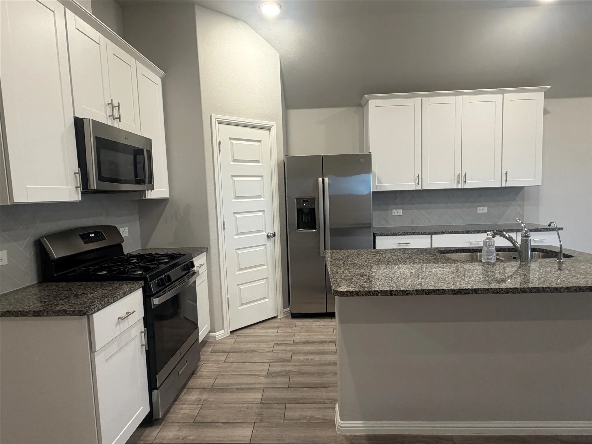 Kitchen featuring white shaker cabinetry, stainless steel appliances, granite countertops, and wood-finish flooring