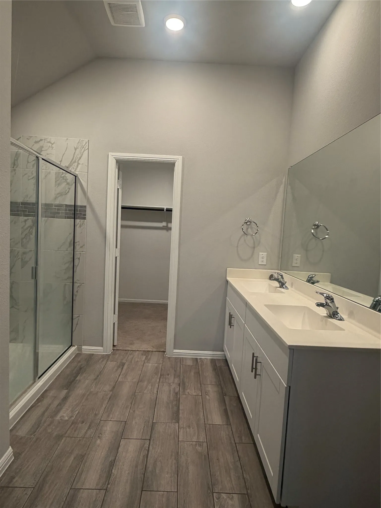 Dual vanity with white cabinetry, wood-finish flooring, glass-enclosed shower with tiled surround, and recessed lighting