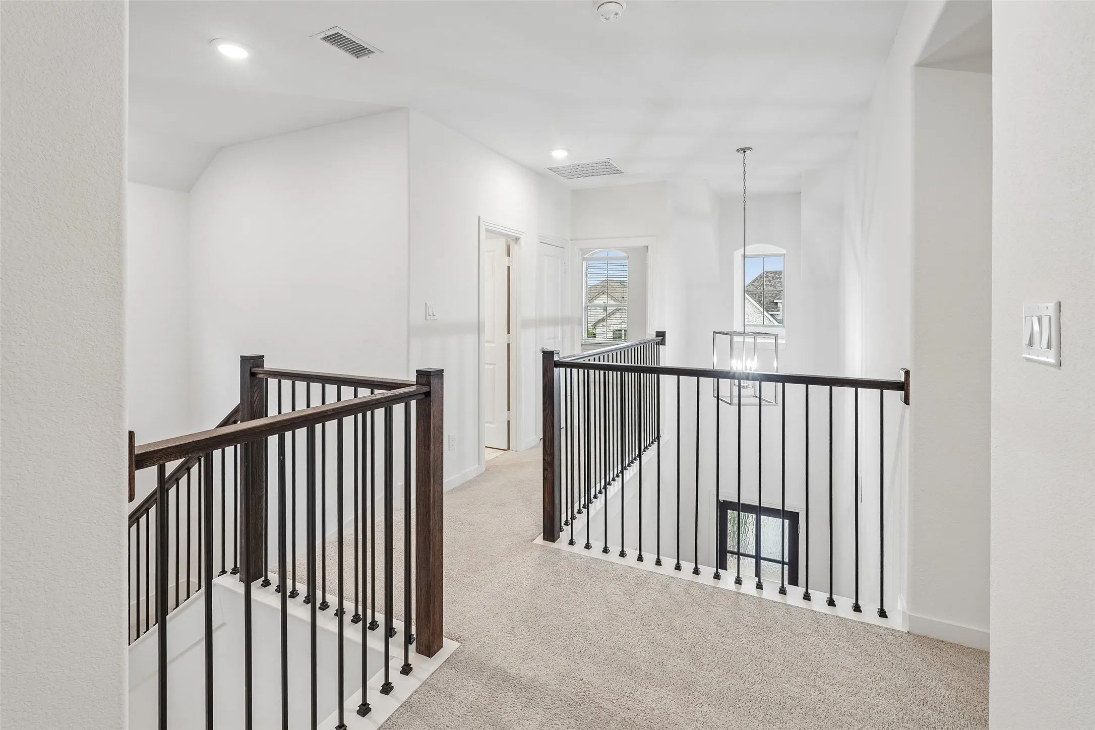 Upper-level landing featuring carpeted flooring, white walls, and a wrought iron and wood-finish railing