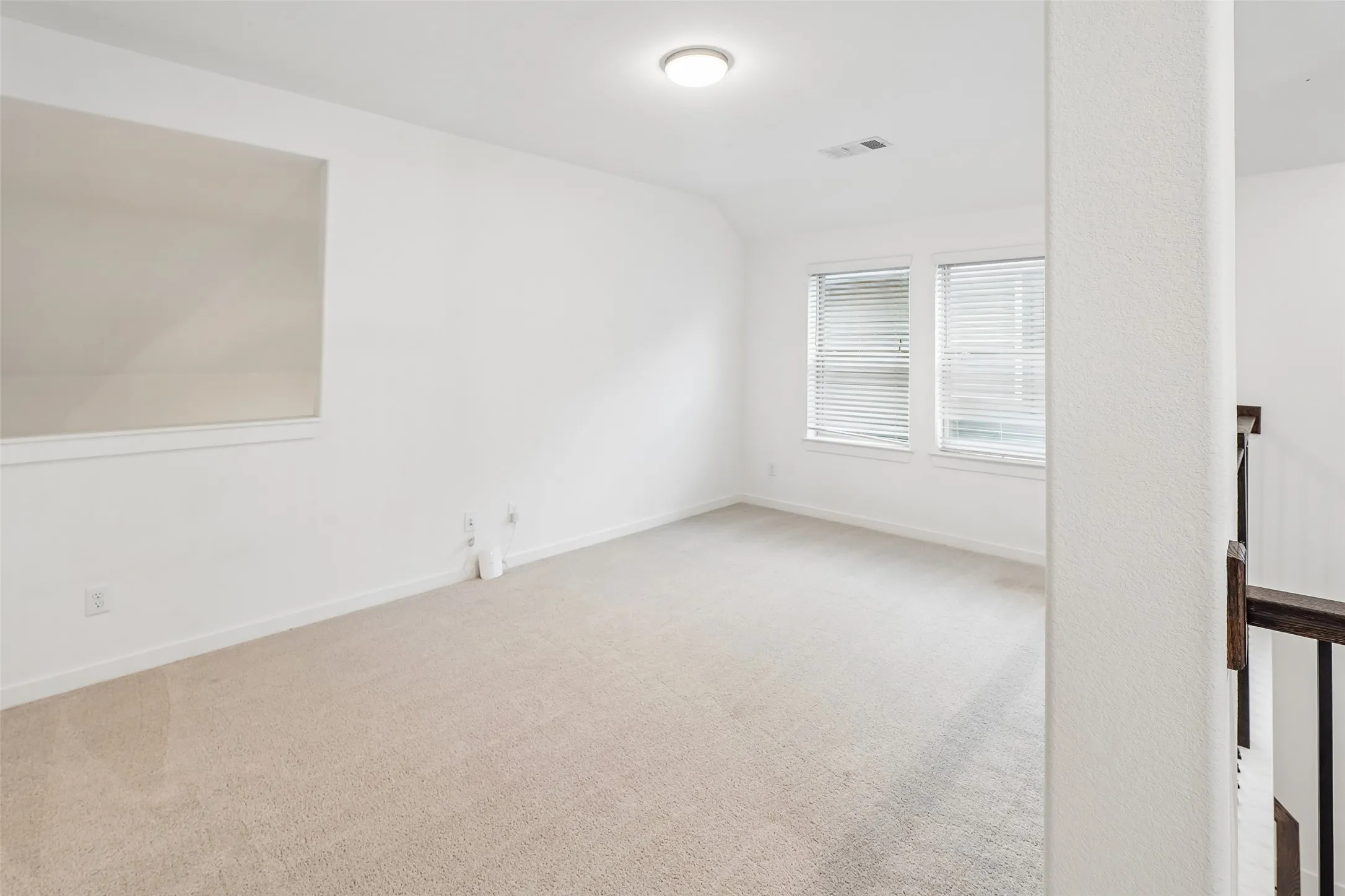 Carpeted room featuring dual windows with blinds, a ceiling-mounted light fixture, and a built-in half wall