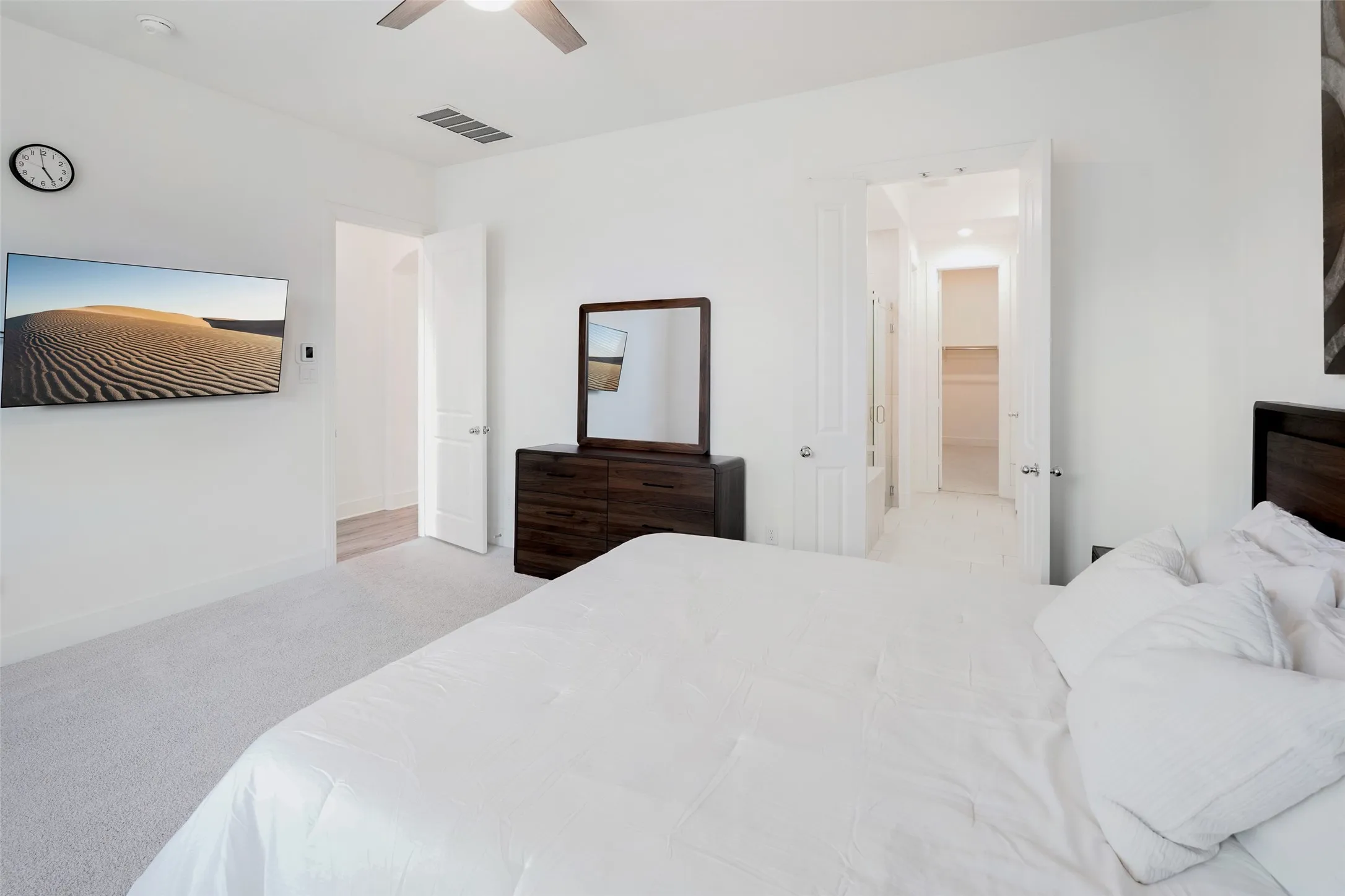 White walls, ceiling fan, carpet flooring, wood-finish flooring, and a walk-in closet with built-in shelving