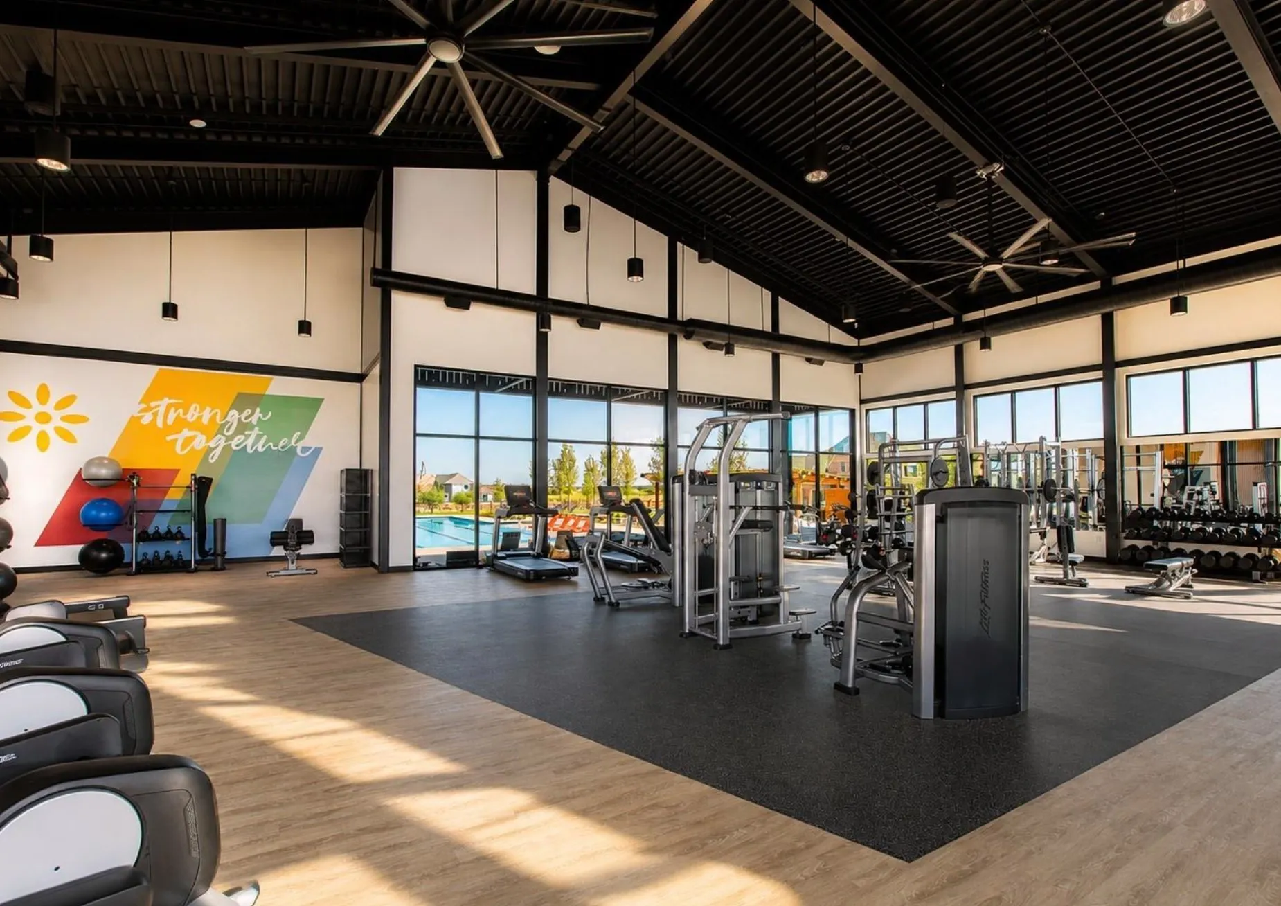 Spacious fitness center featuring vaulted ceilings, exposed structural beams, full-height windows, a large ceiling fan, and mixed flooring surfaces