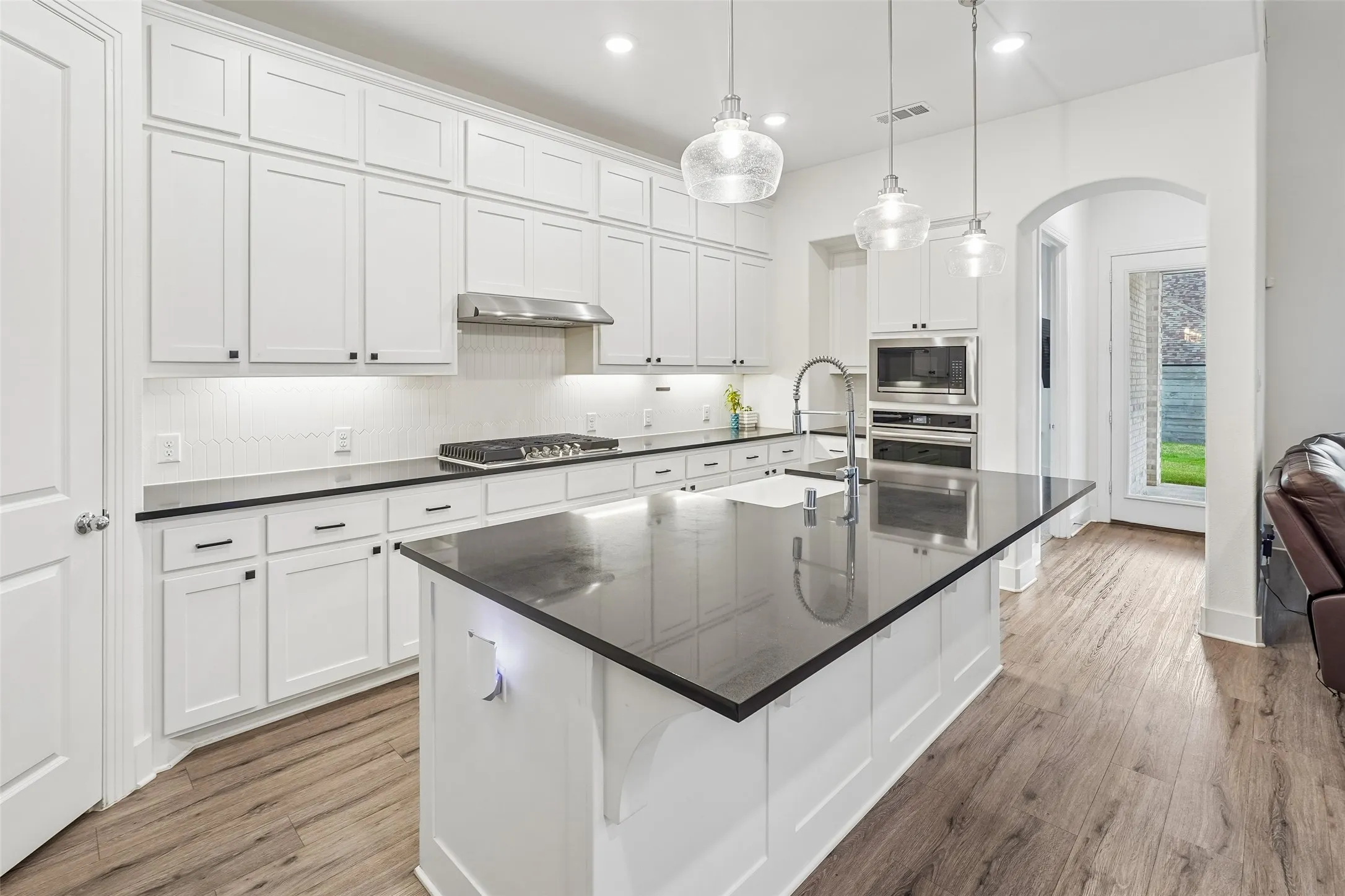 Kitchen featuring white shaker cabinetry, dark countertops, wood-finish flooring, stainless steel appliances, and a central island with an undermount sink