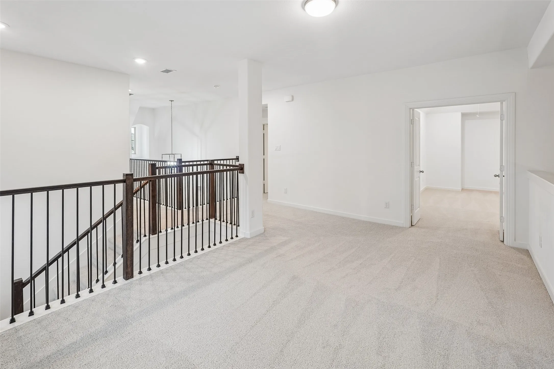 Expansive carpeted loft area featuring a wrought iron and wood-finish railing, recessed lighting, and a neutral color palette