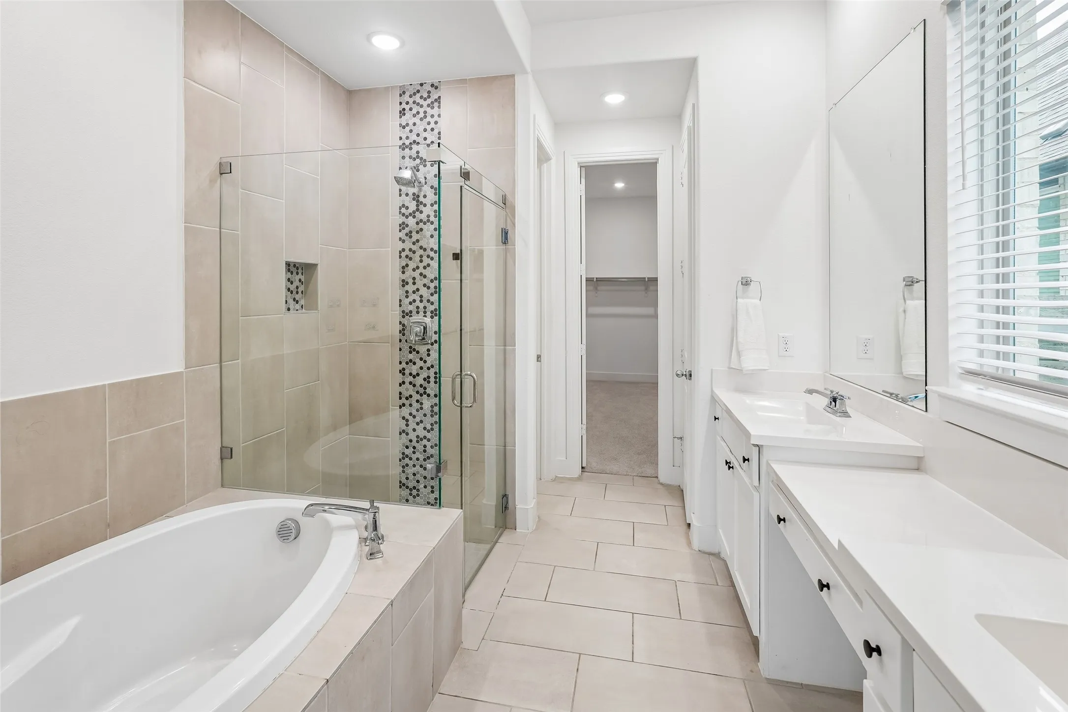 Soaking tub with tile surround, glass-enclosed shower featuring a mosaic tile accent, dual vanity with undermount sinks, and a built-in vanity area