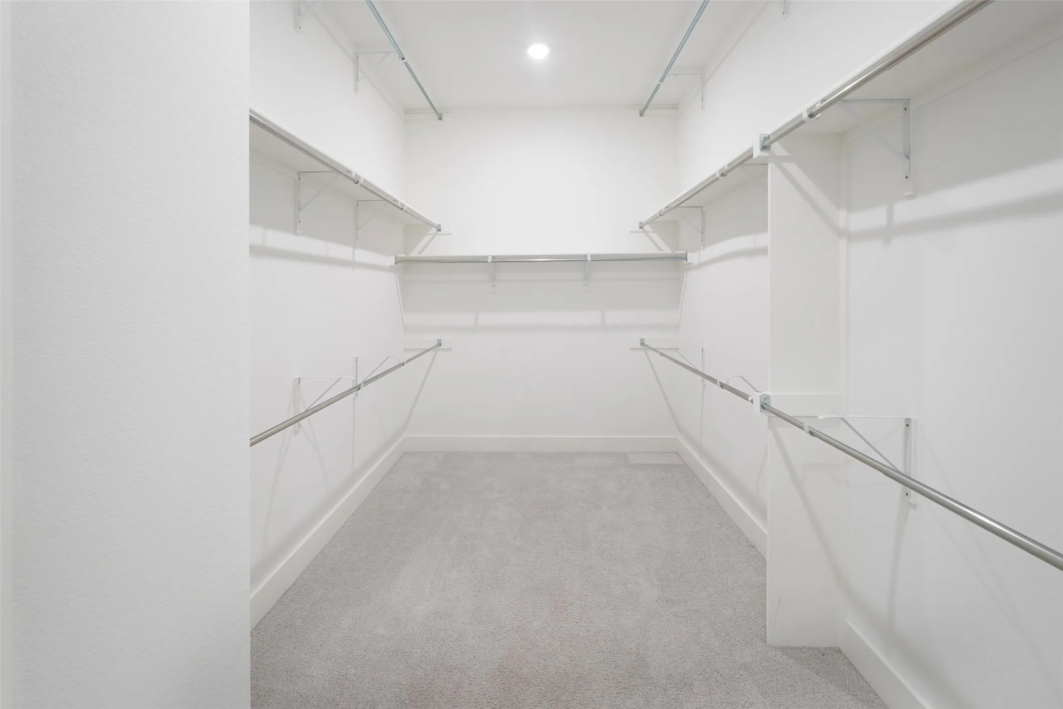 Walk-in closet featuring white shelving, multiple hanging rods, recessed lighting, and light grey carpeting