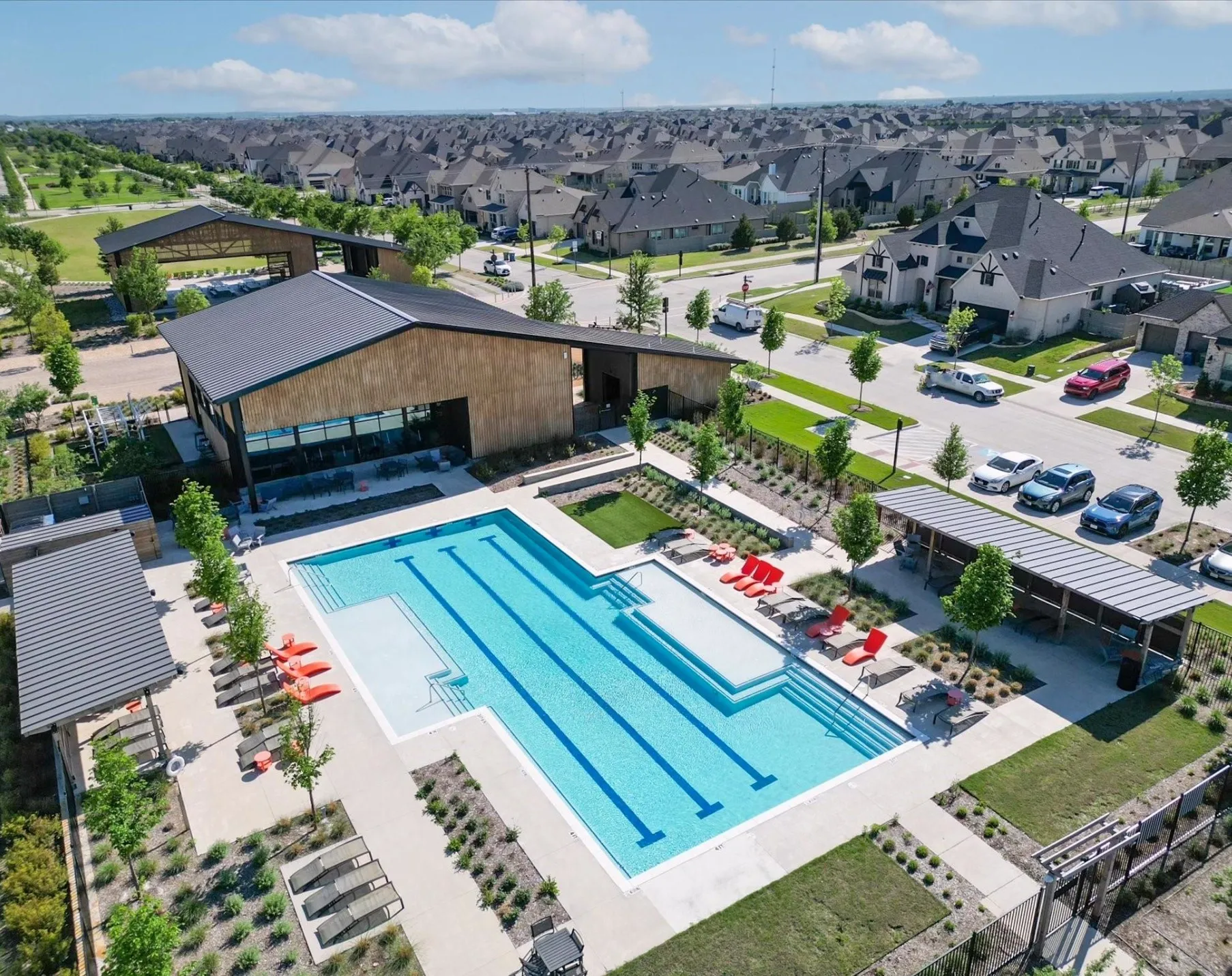 Community swimming pool with lap lanes, expansive pool deck, and a modern clubhouse with wood-finish siding