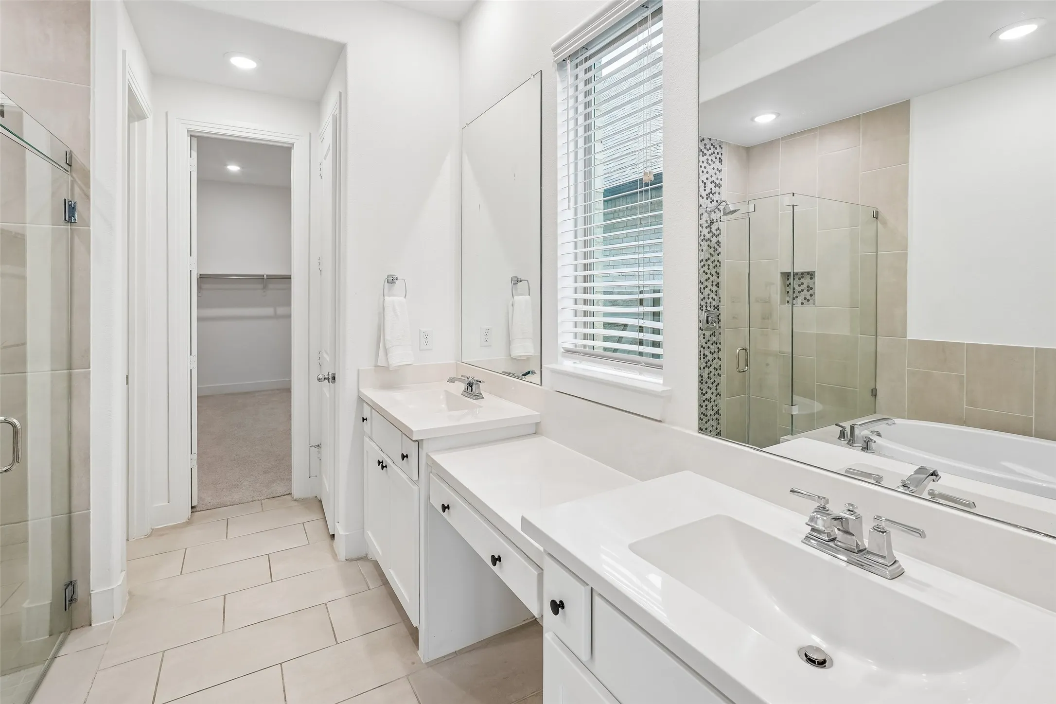 Dual vanity with integrated sinks, built-in makeup counter, glass-enclosed shower, and a soaking tub