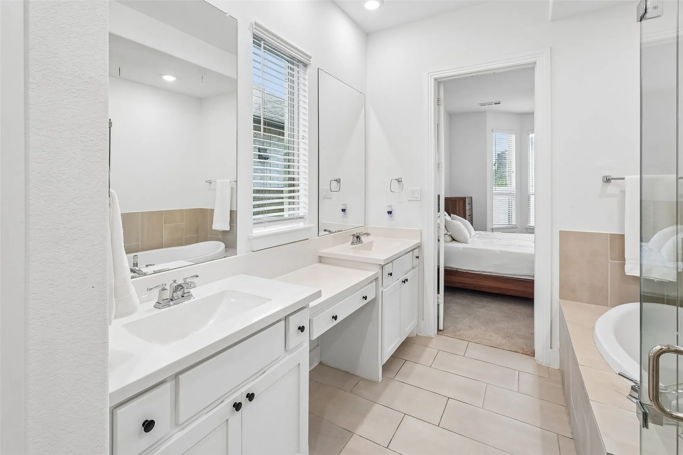 Dual vanity with undermount sinks, white cabinetry, integrated makeup counter, and a soaking tub with tile surround