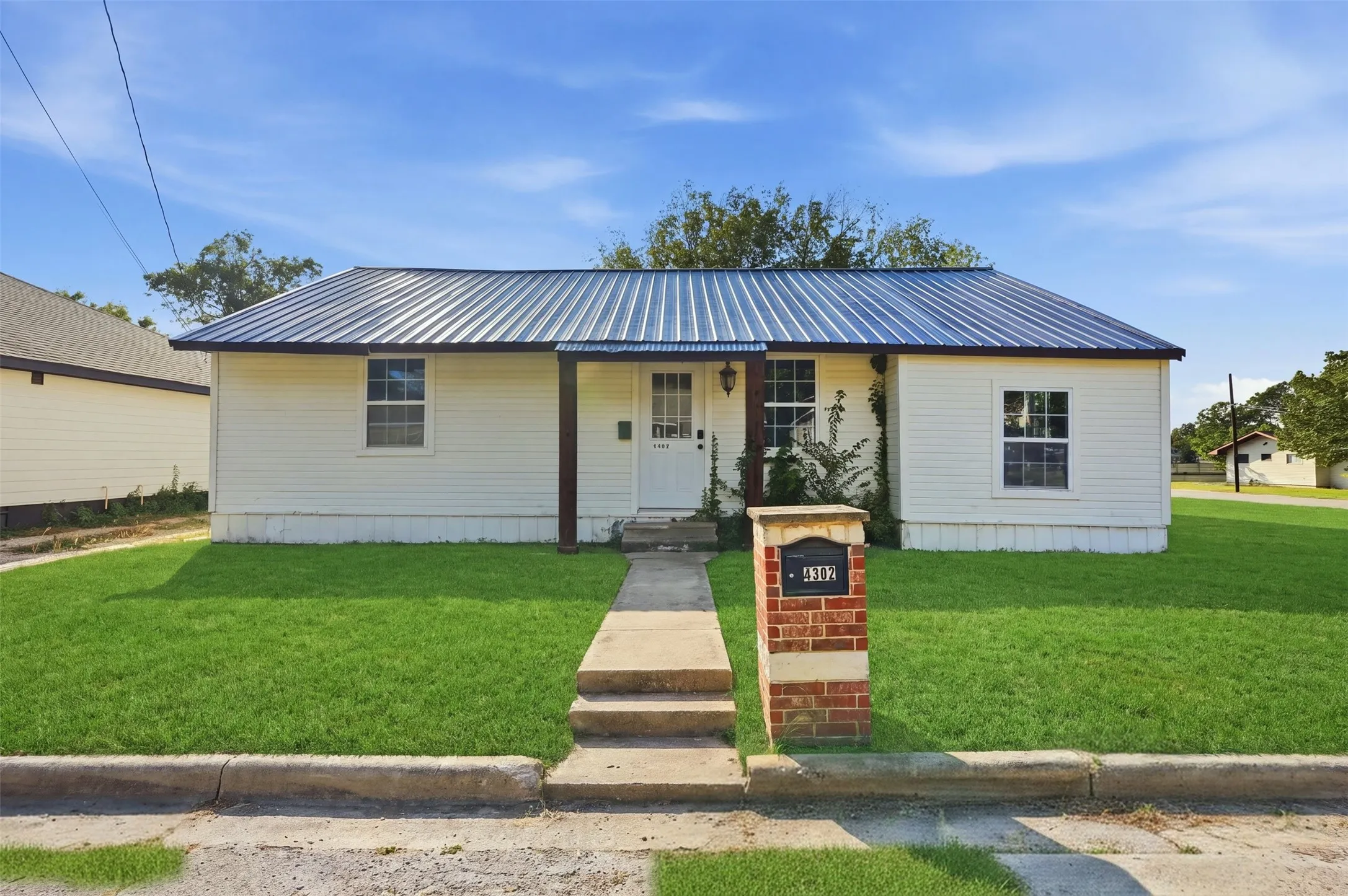 White siding exterior with a dark metal roof, featuring a covered entry porch