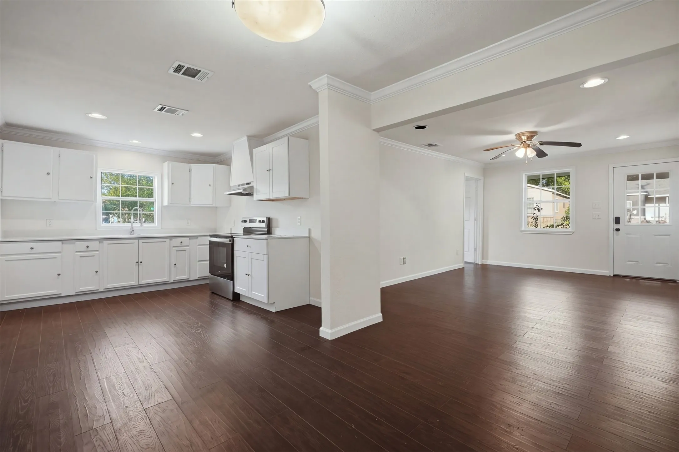 Wood-finish flooring throughout, bright white kitchen cabinetry, stainless steel range and hood, recessed lighting, and a ceiling fan